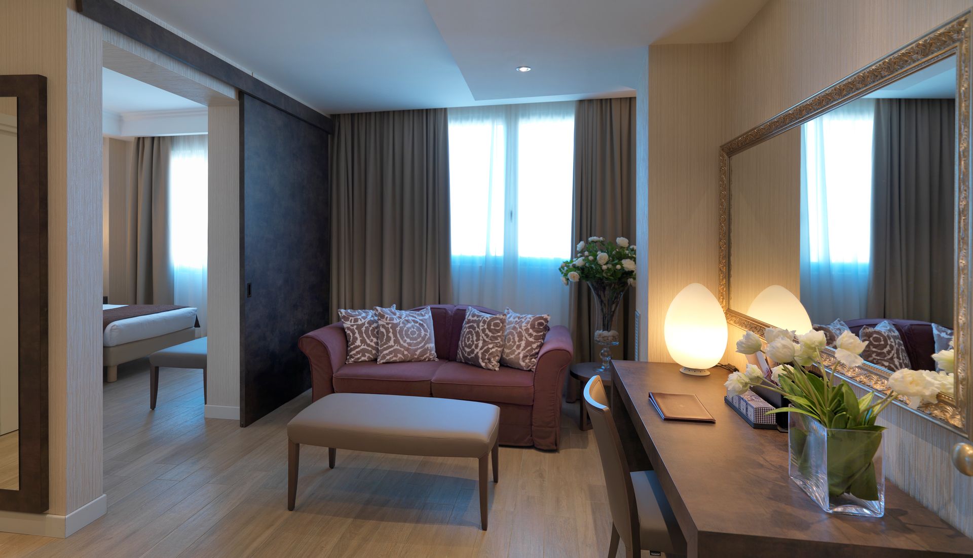 Habitación de hotel moderna con sofá, escritorio, espejo, cama y ventana grande.