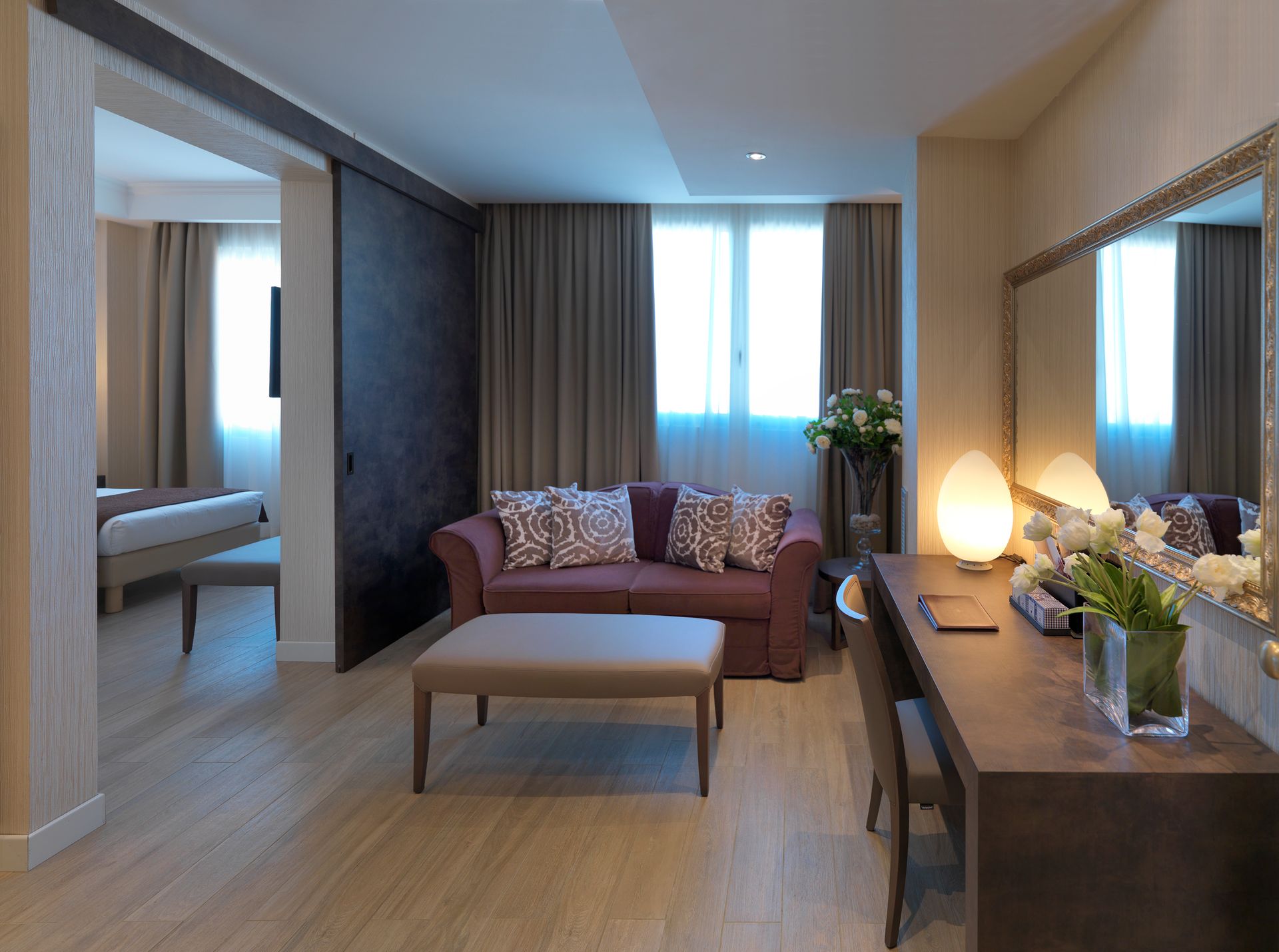 Suite de hotel moderna con sofá, mesa de centro, escritorio e iluminación cálida.