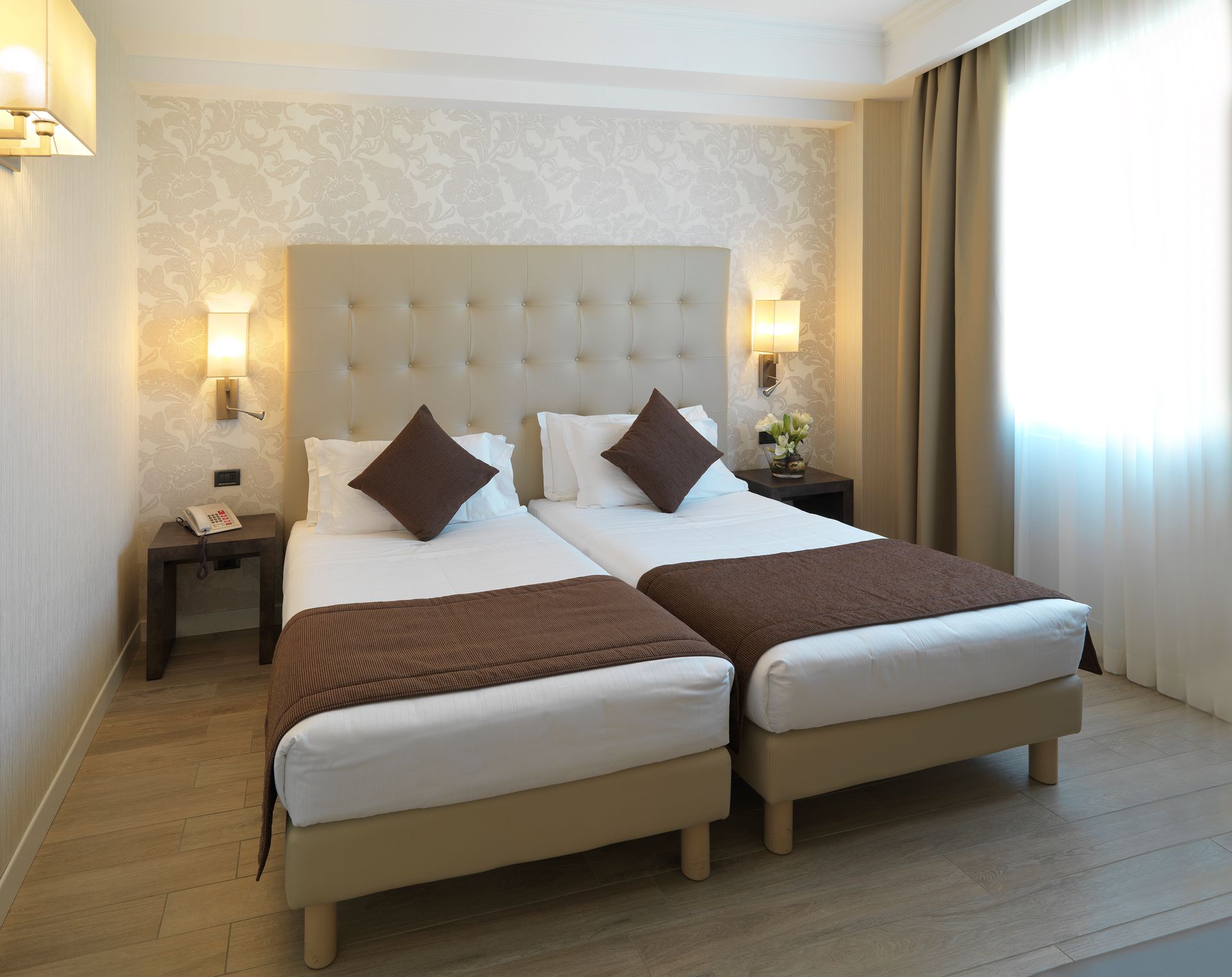 Habitación de hotel luminosa con dos camas individuales, decoración en tonos beige, lámparas de pared