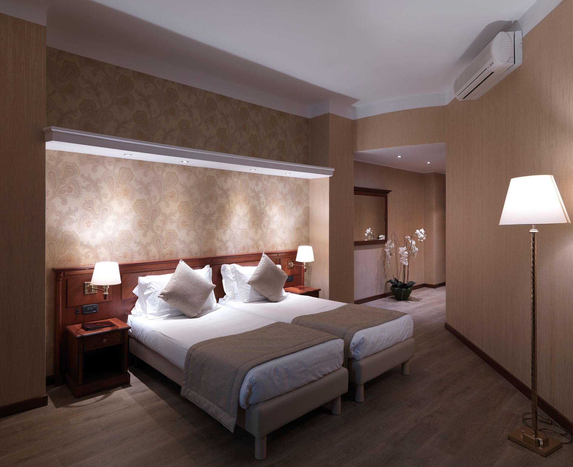 Habitación de hotel moderna con dos camas blancas, paredes de color beige cálido, lámparas y una lámpara de pie.