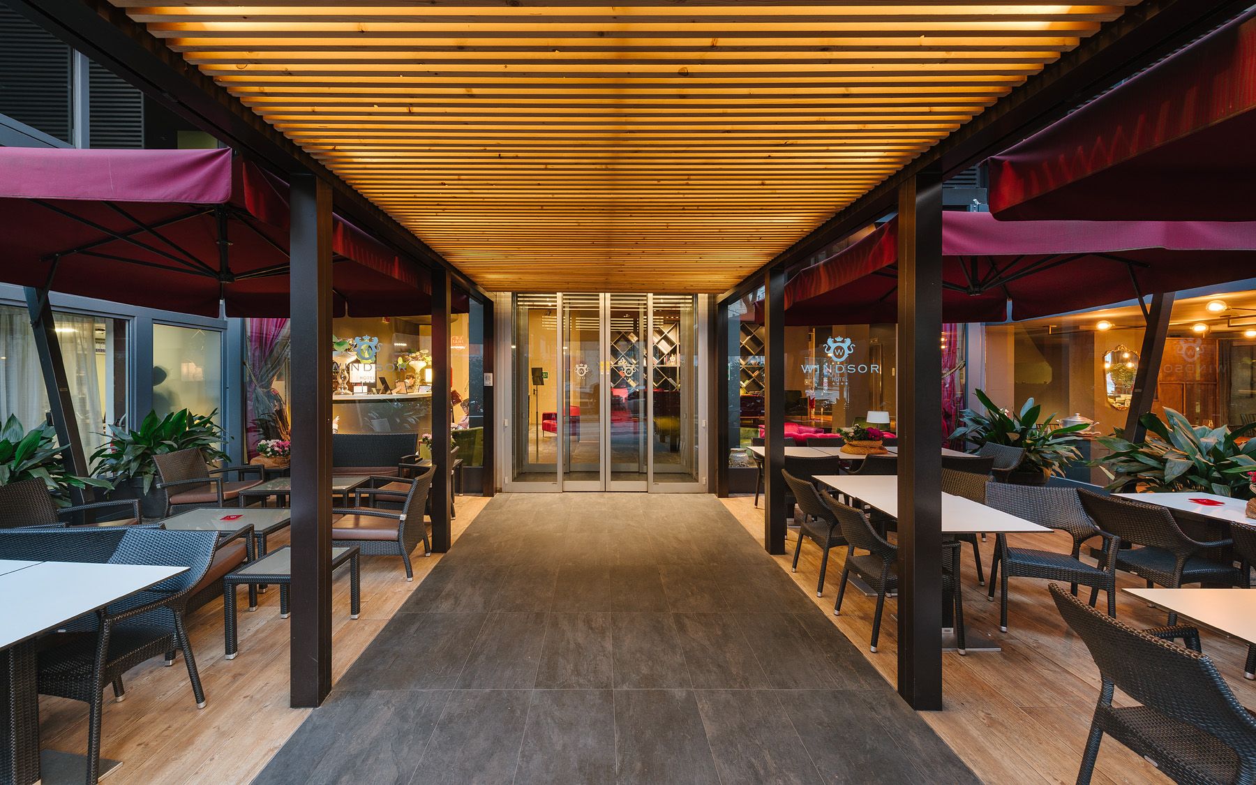 Patio exterior cubierto del restaurante con mesas, sillas e iluminación cálida en el techo de madera.