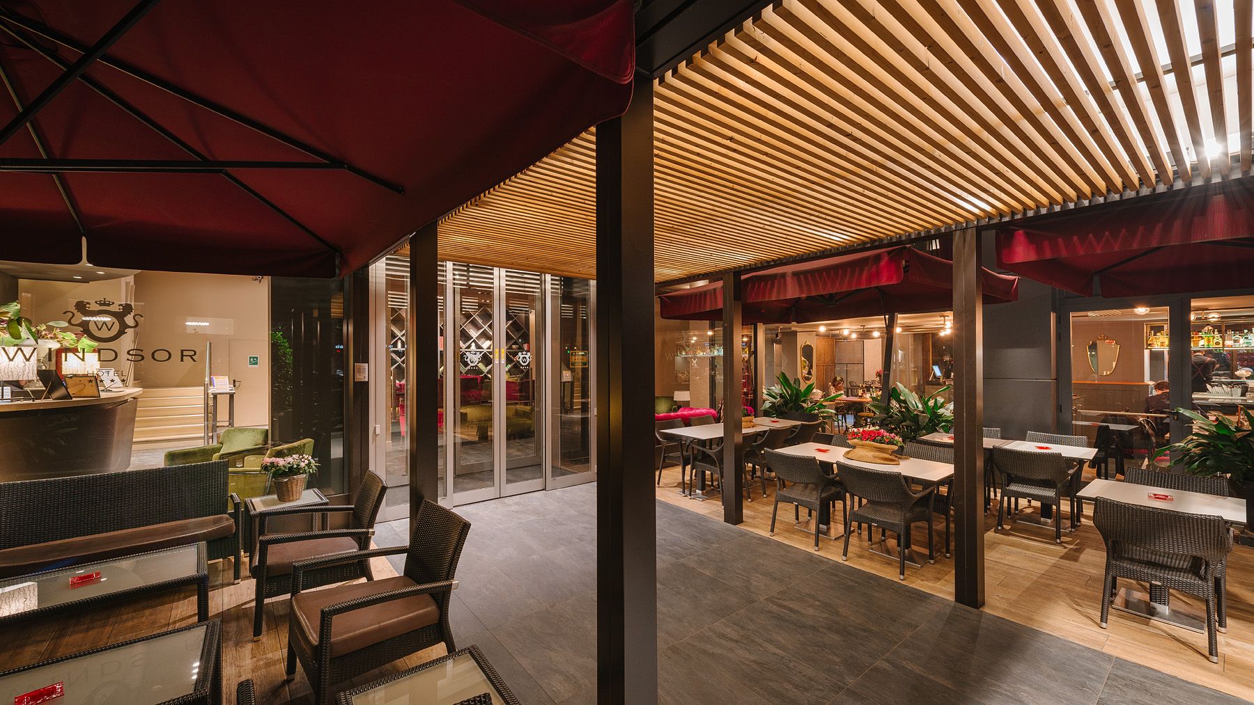 Terraza exterior del restaurante con mesas, sillas y toldos a rayas iluminados cálidamente al atardecer.