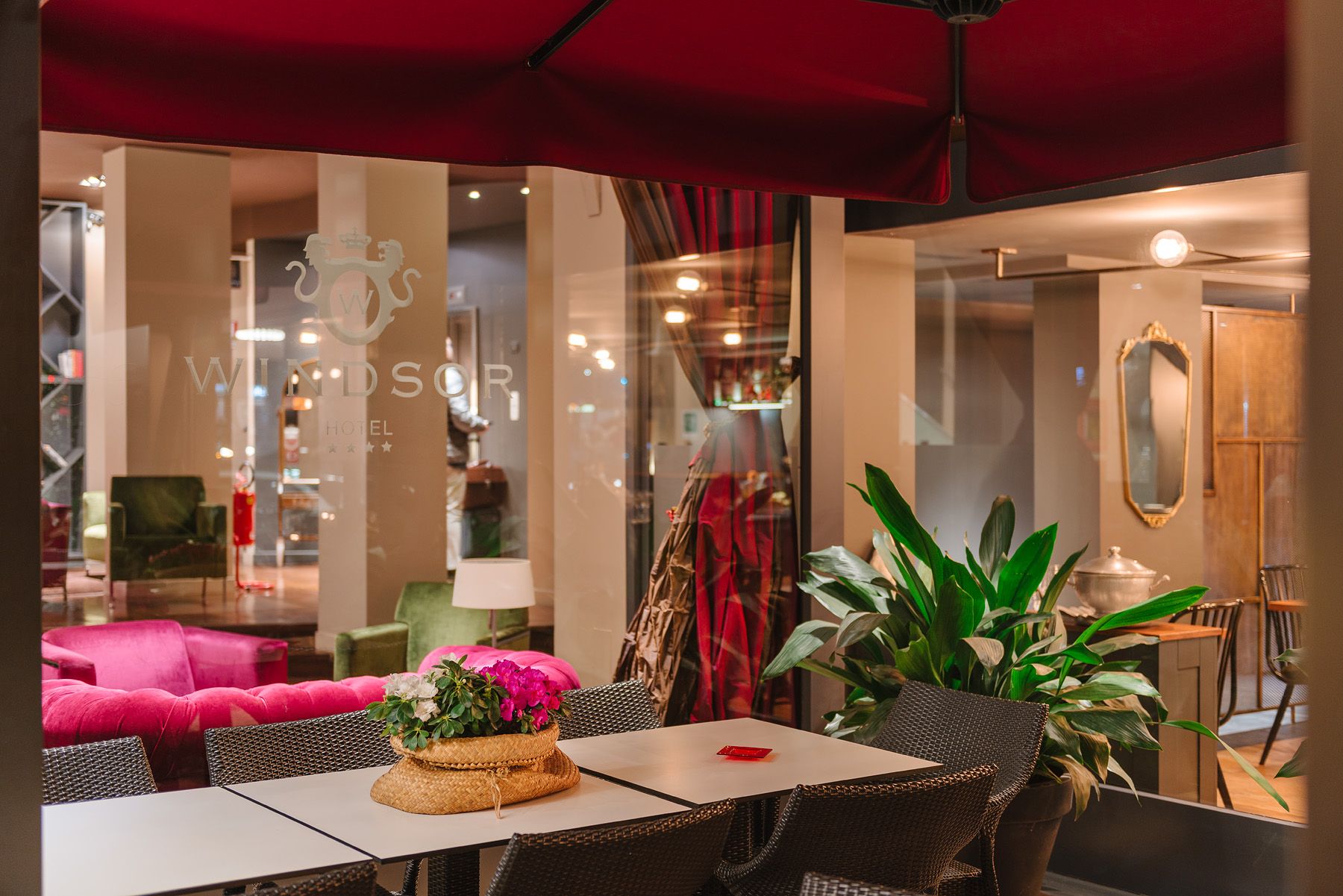 Interior de cafetería con estilo, con toldos rojos, sillas blancas, plantas y asientos rosas cerca de una mesa.