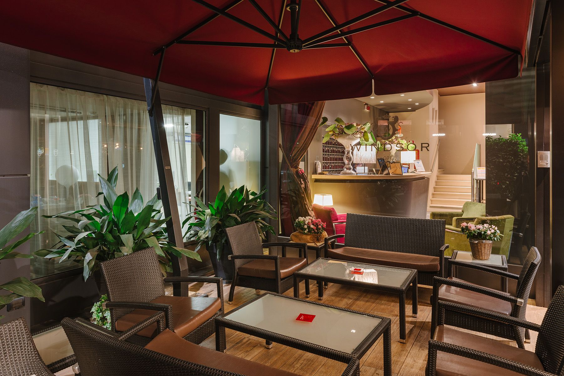 Acogedor salón al aire libre con toldo rojo, sillas de mimbre, plantas en macetas y una mesa bañada por la cálida luz