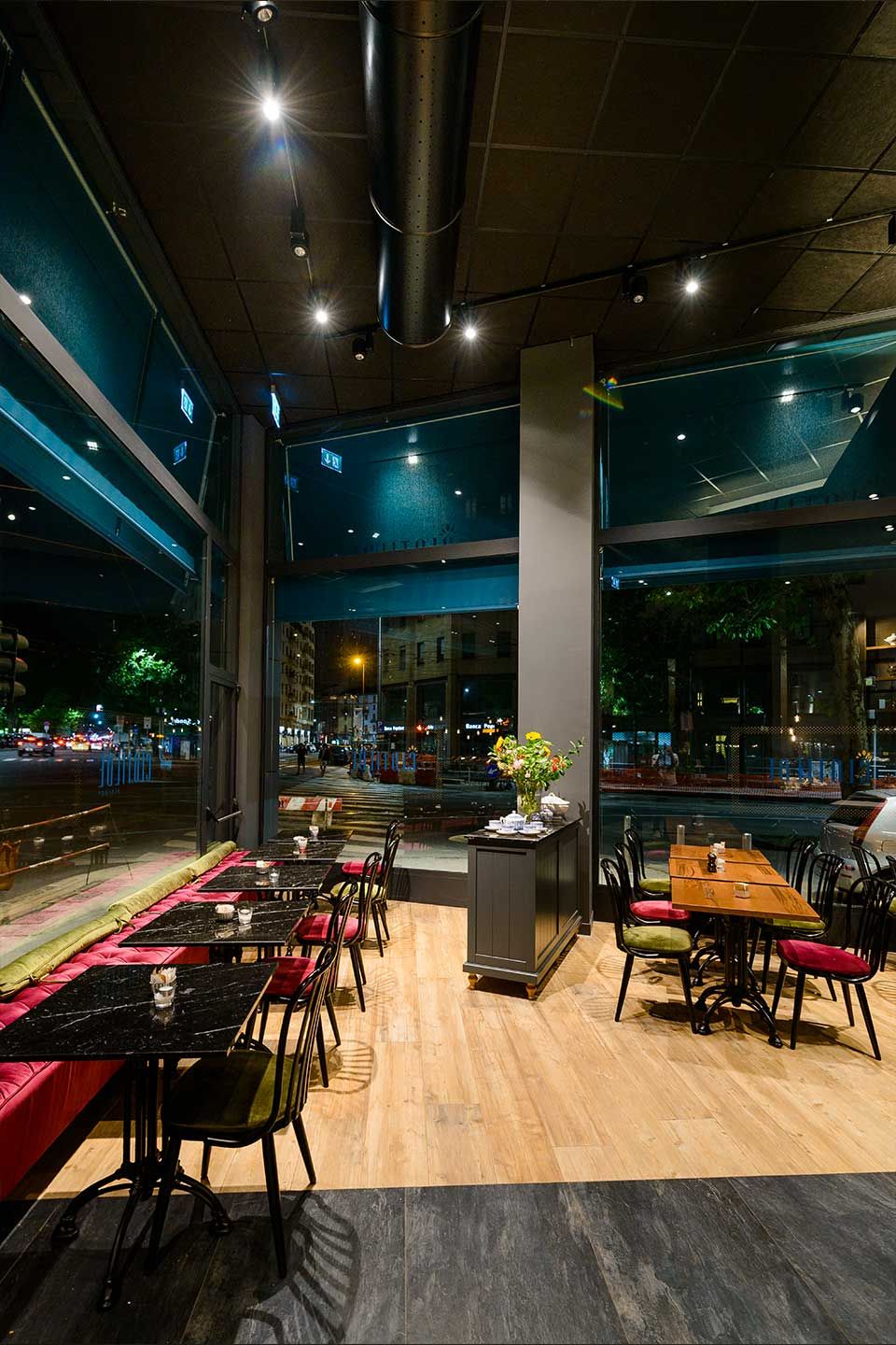 Comedor moderno con mesas, sillas y una pared de cristal por la noche.