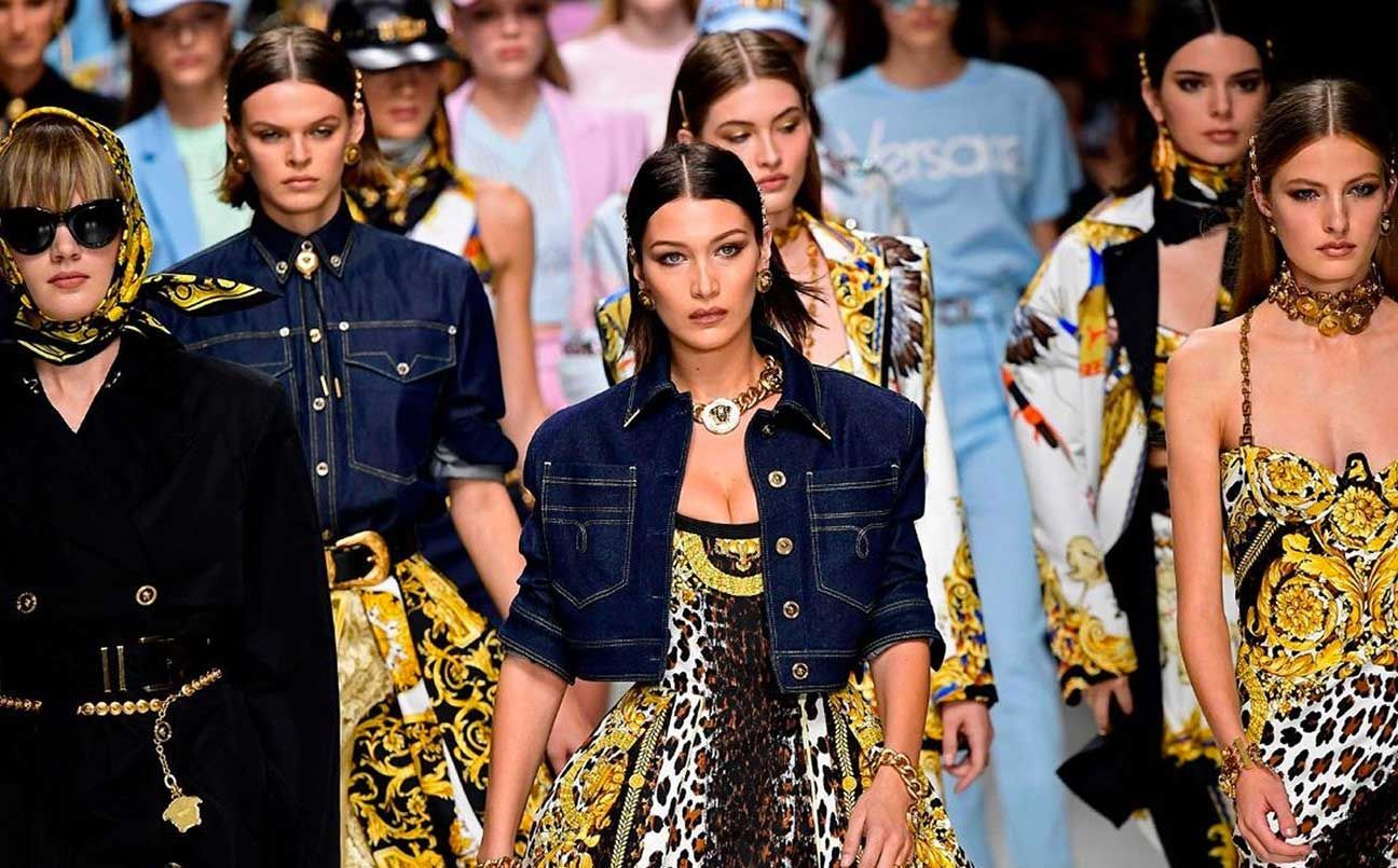 Modelli che sfilano in passerella con abiti dai motivi audaci e giacche di jeans durante una sfilata di moda.