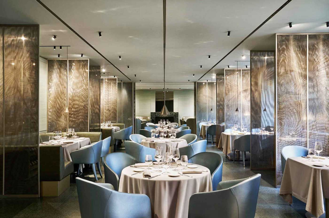 Elegante sala da pranzo del ristorante con tavoli rotondi, sedie blu e luci decorative calde.