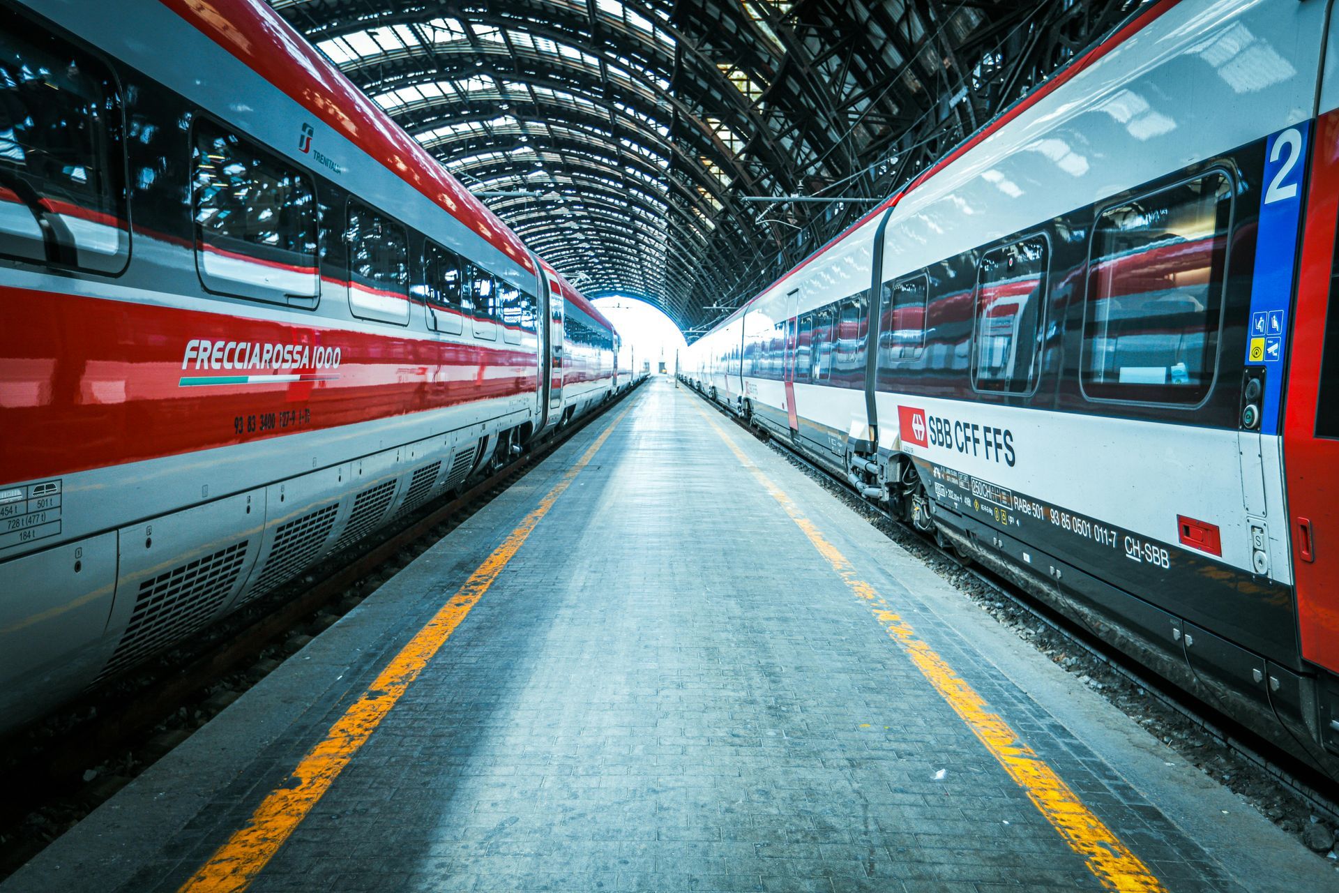 Due treni ad alta velocità su una banchina coperta di una stazione, visti dal corridoio centrale.