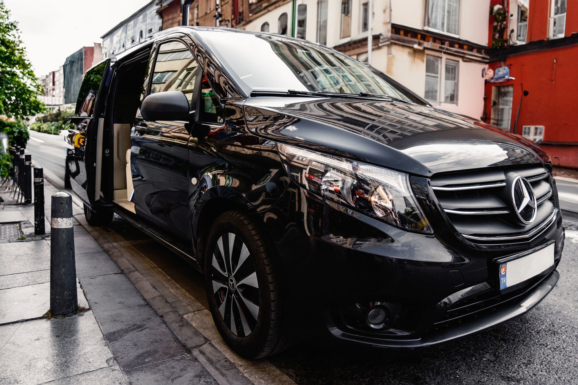 Black Mercedes van parked on a wet city street beside buildings and bollards