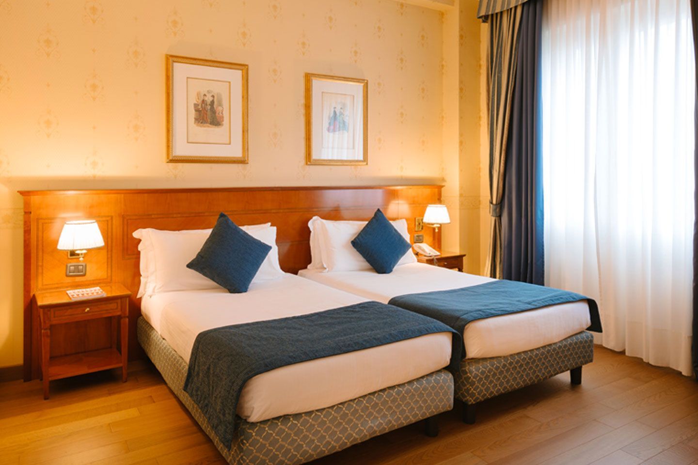 Accogliente camera d'albergo con due letti singoli, biancheria da letto blu, calde tonalità del legno e una finestra