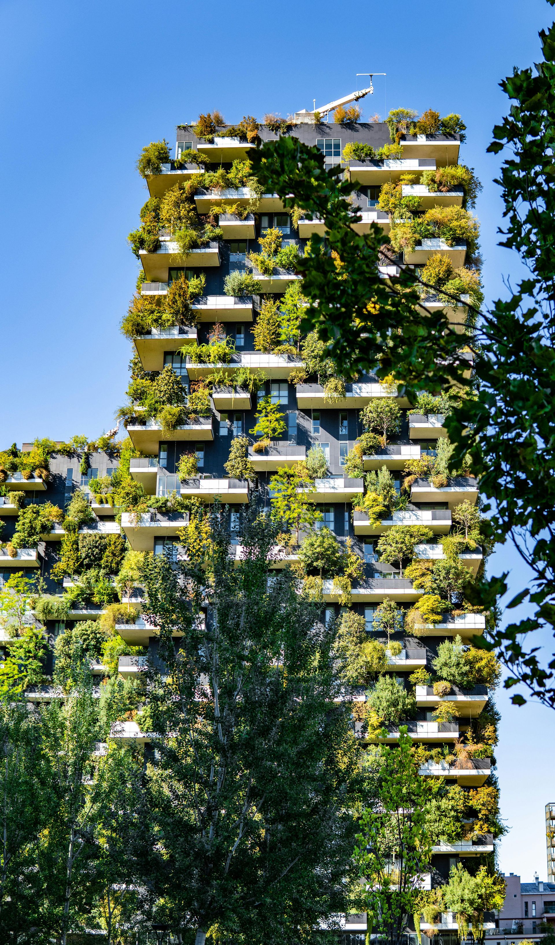 Alta torre moderna cubierta de vegetación y balcones contra un cielo azul.