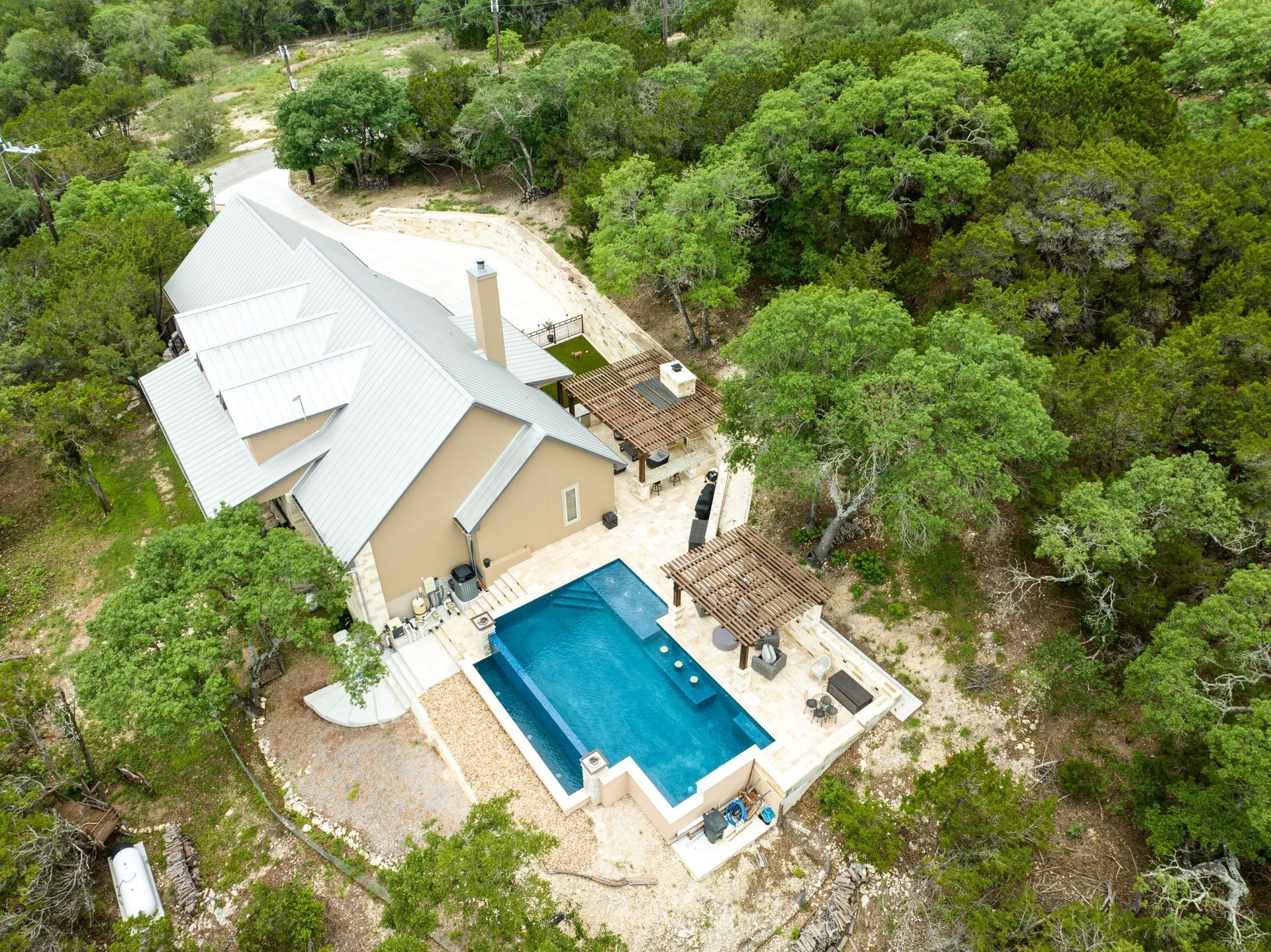 An aerial view of a house with a large swimming pool surrounded by trees built by Fine Patio Design San Antonio TX