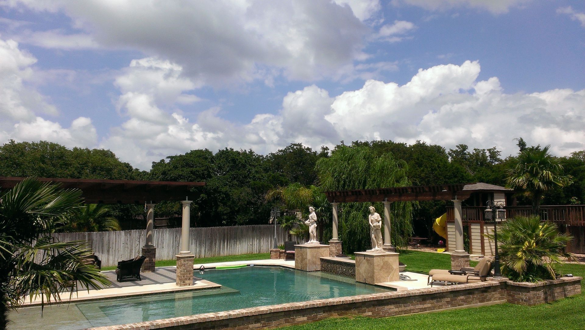 A large swimming pool surrounded by statues on a sunny day designed by Fine Patio Design San Antonio TX