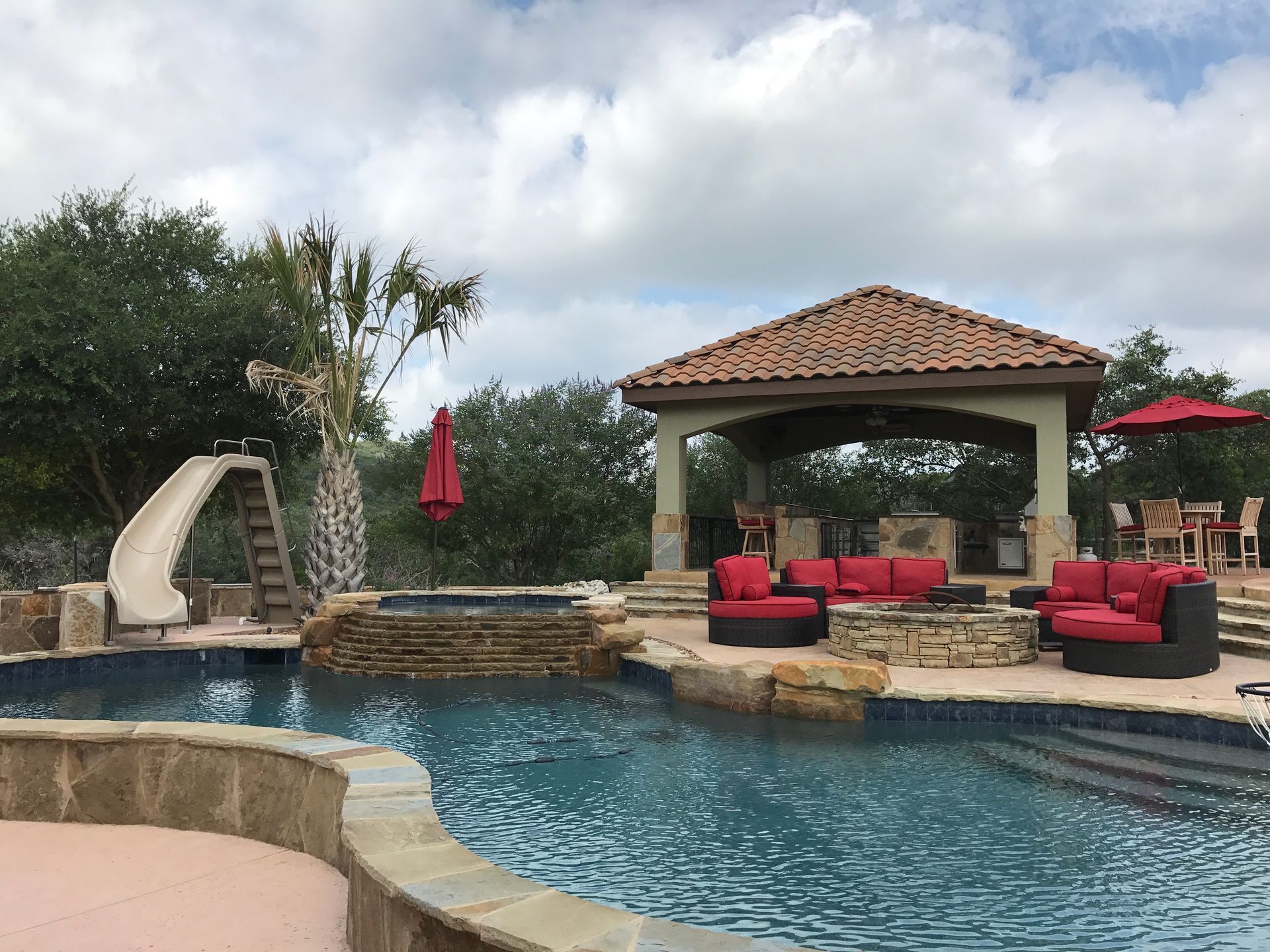 A large swimming pool with a slide and a gazebo designed by Fine Patio Design San Antonio TX