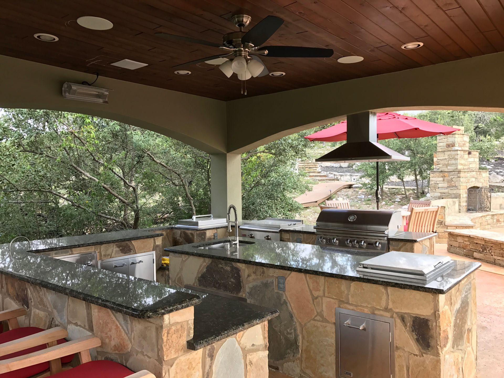 An outdoor kitchen with a ceiling fan and umbrellas built by Fine Patio Design San Antonio TX