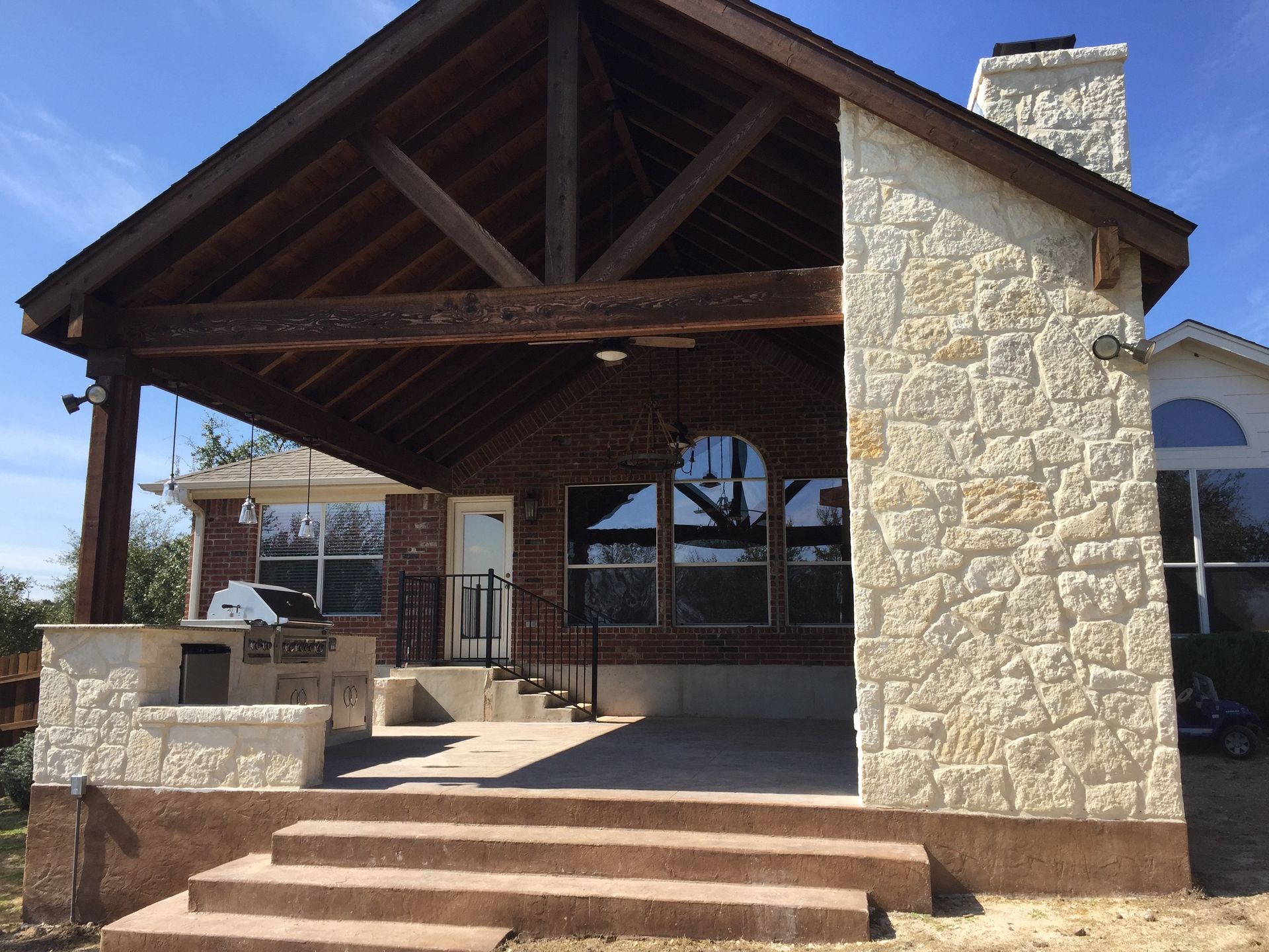 A house with a stone wall and a wooden roof built by Fine Patio Design San Antonio TX