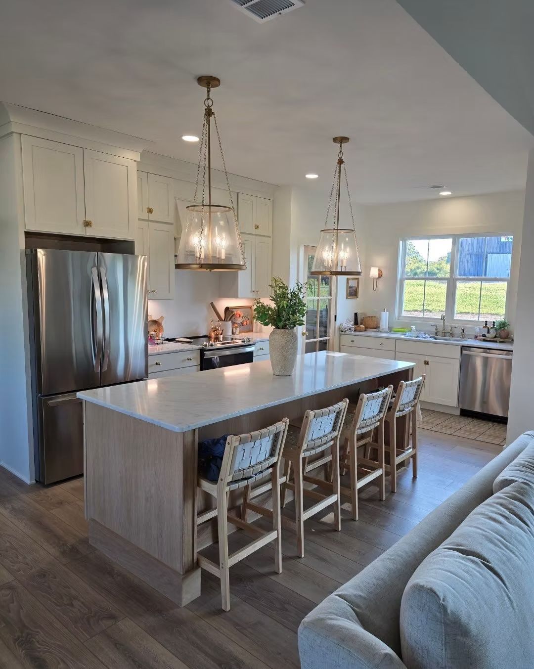 Bright modern kitchen with island, barstools, stainless fridge, pendant lights, and large window.