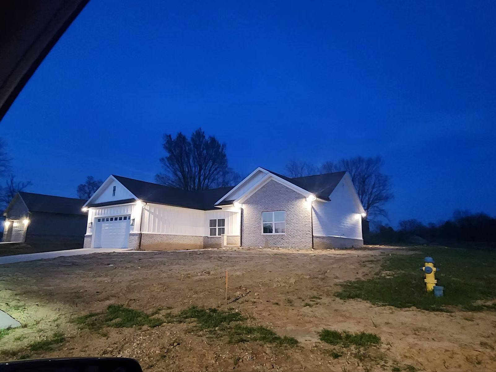 New house at dusk with lit exterior lights and a yellow fire hydrant in the foreground