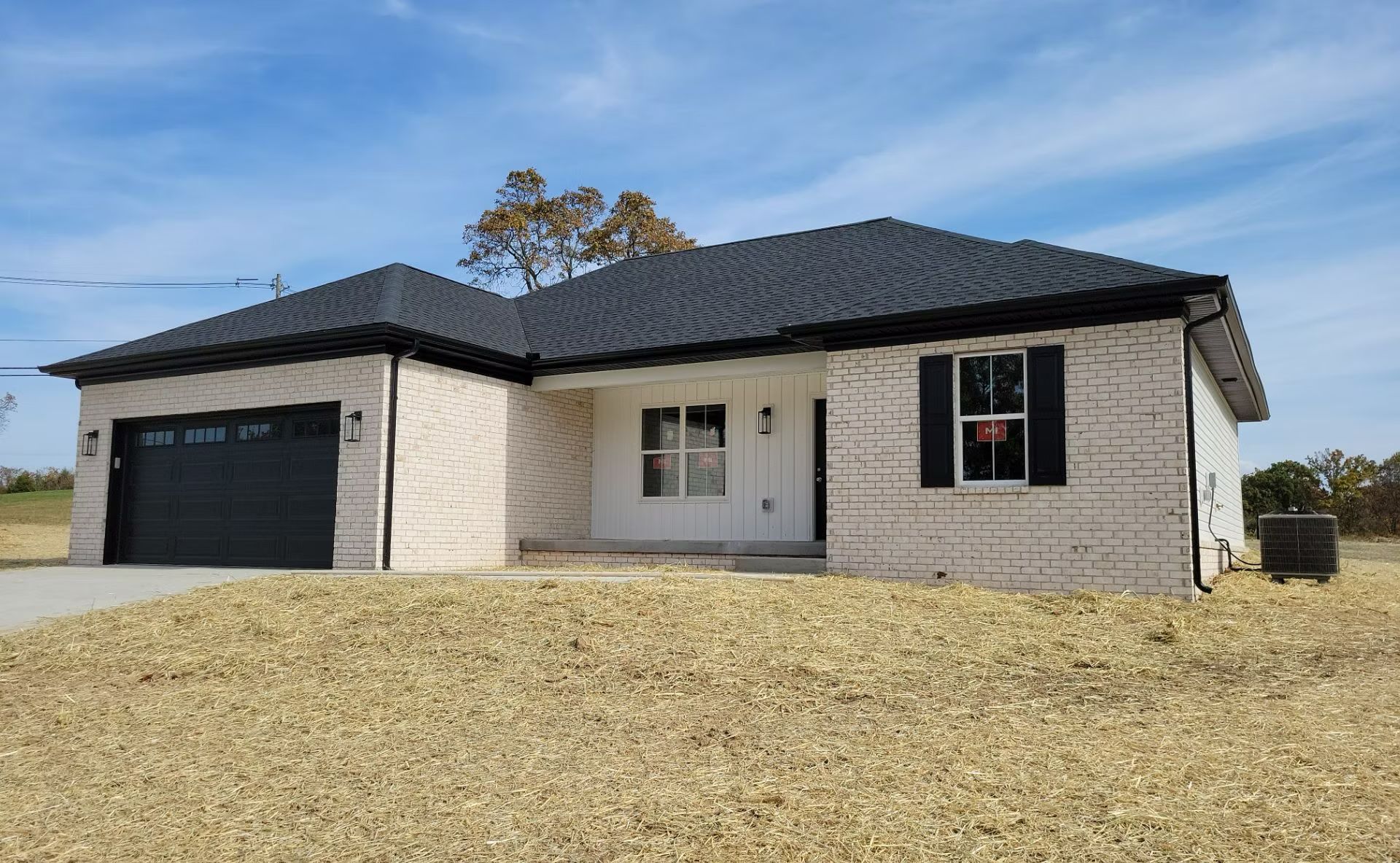 Single-story brick house with black roof, garage, and gravel driveway under a clear sky