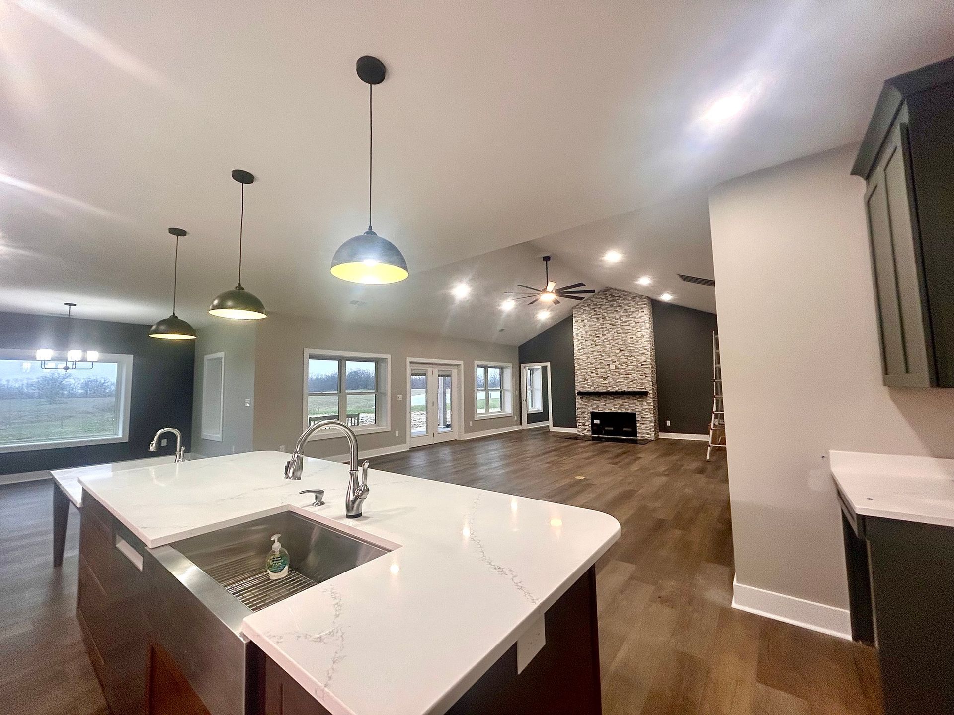 Modern open-concept kitchen with white island, pendant lights, hardwood floors, and stone fireplace in the background