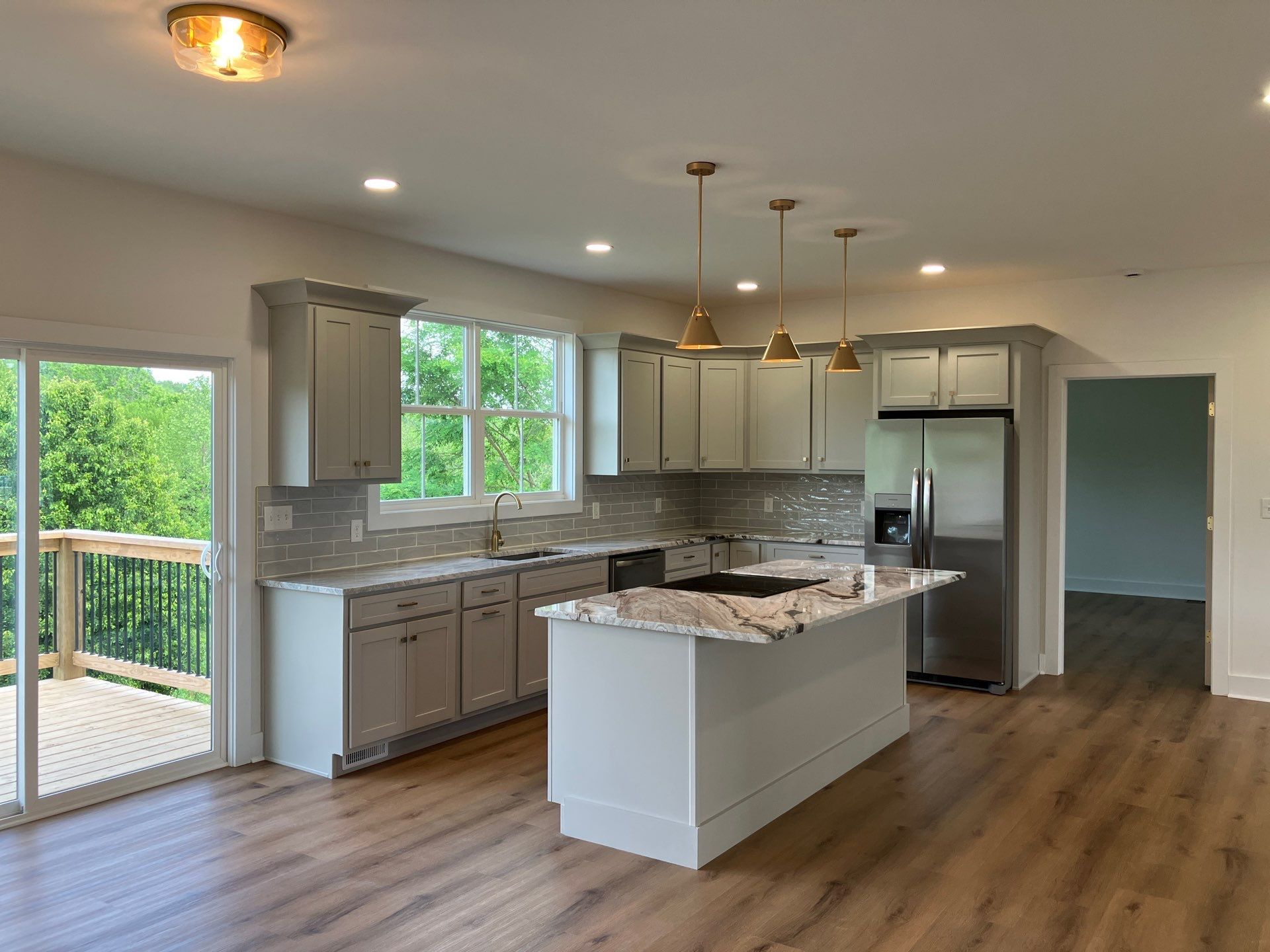 Modern kitchen with island, stainless steel appliances, wood floors, and large windows overlooking a deck
