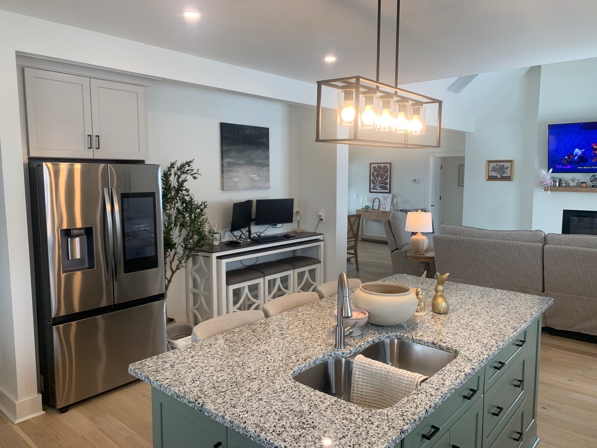 Modern kitchen with granite island, stainless fridge, and open living area beyond.