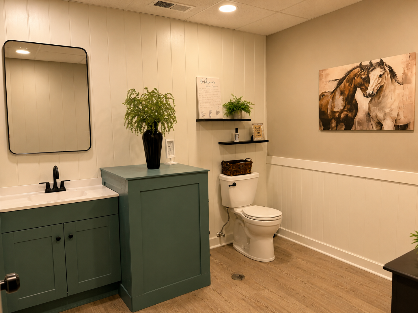 Modern bathroom with green vanity, toilet, wall art, and potted plants on beige walls and wood floor