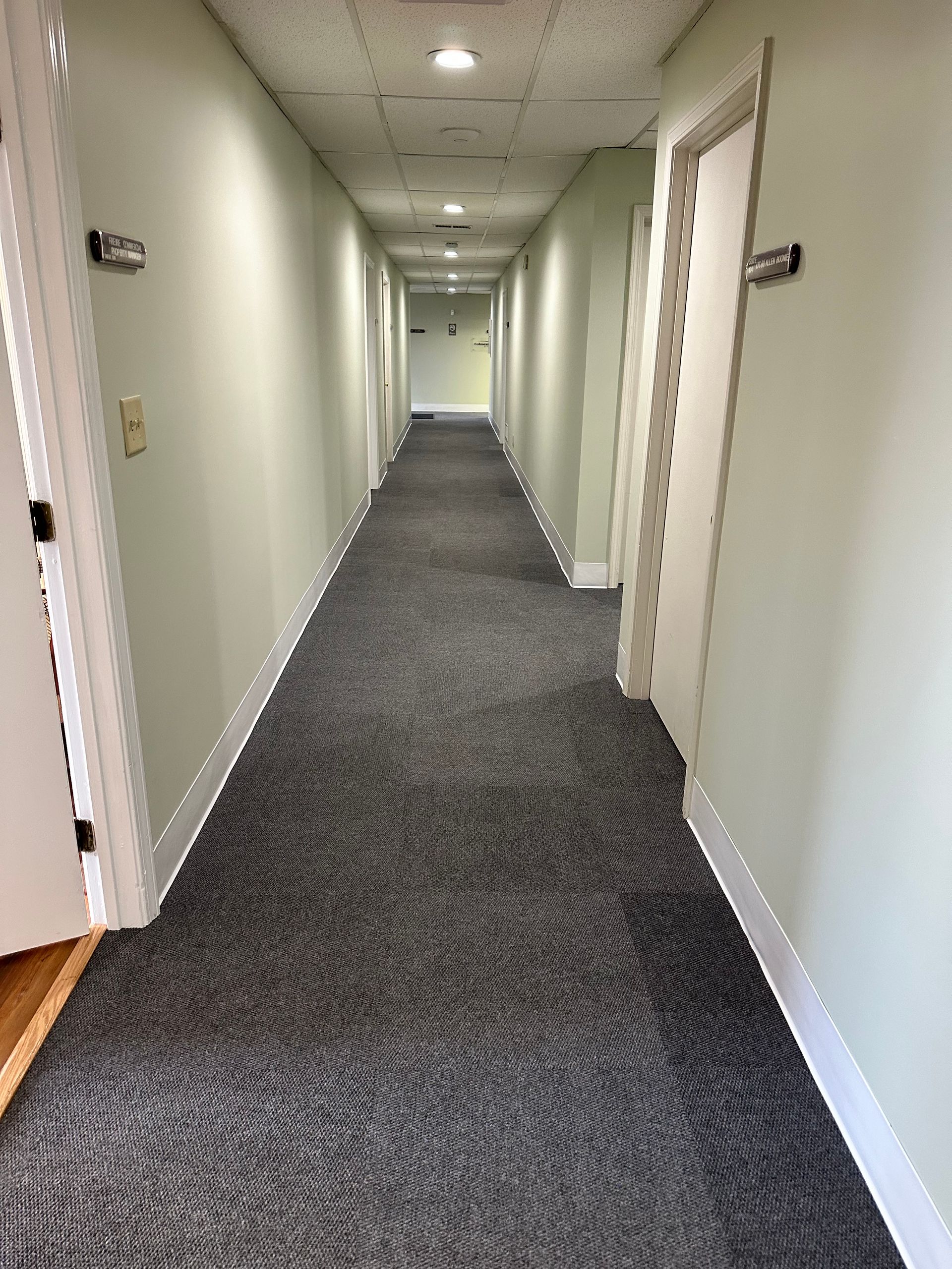 Long indoor hallway with white walls, gray carpet, and doors along both sides.