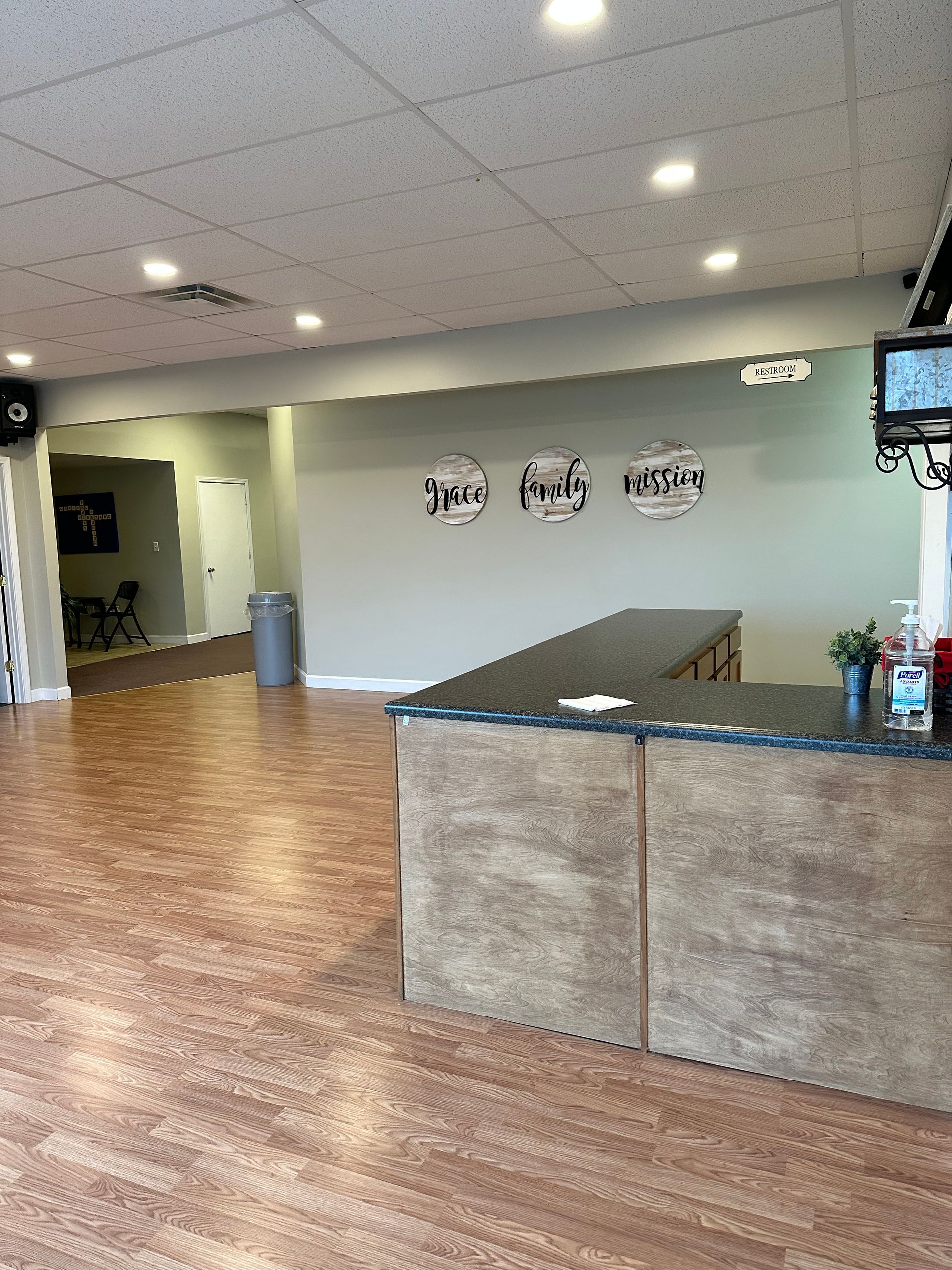 Empty lobby with wood floor, gray walls, front counter, and ceiling lights in a fitness or salon space