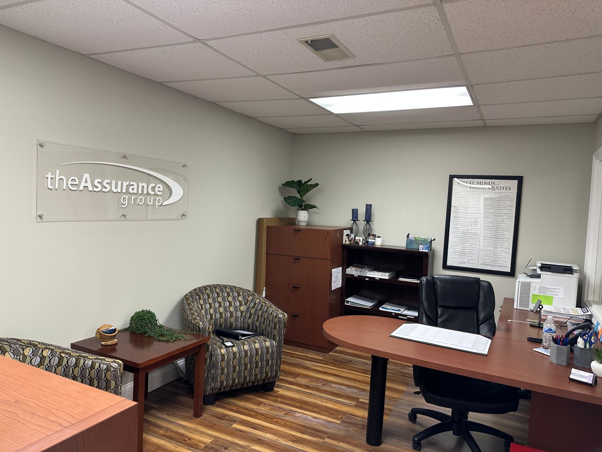 Office interior with desk, chairs, filing cabinet, and wall sign reading “The Assurance”