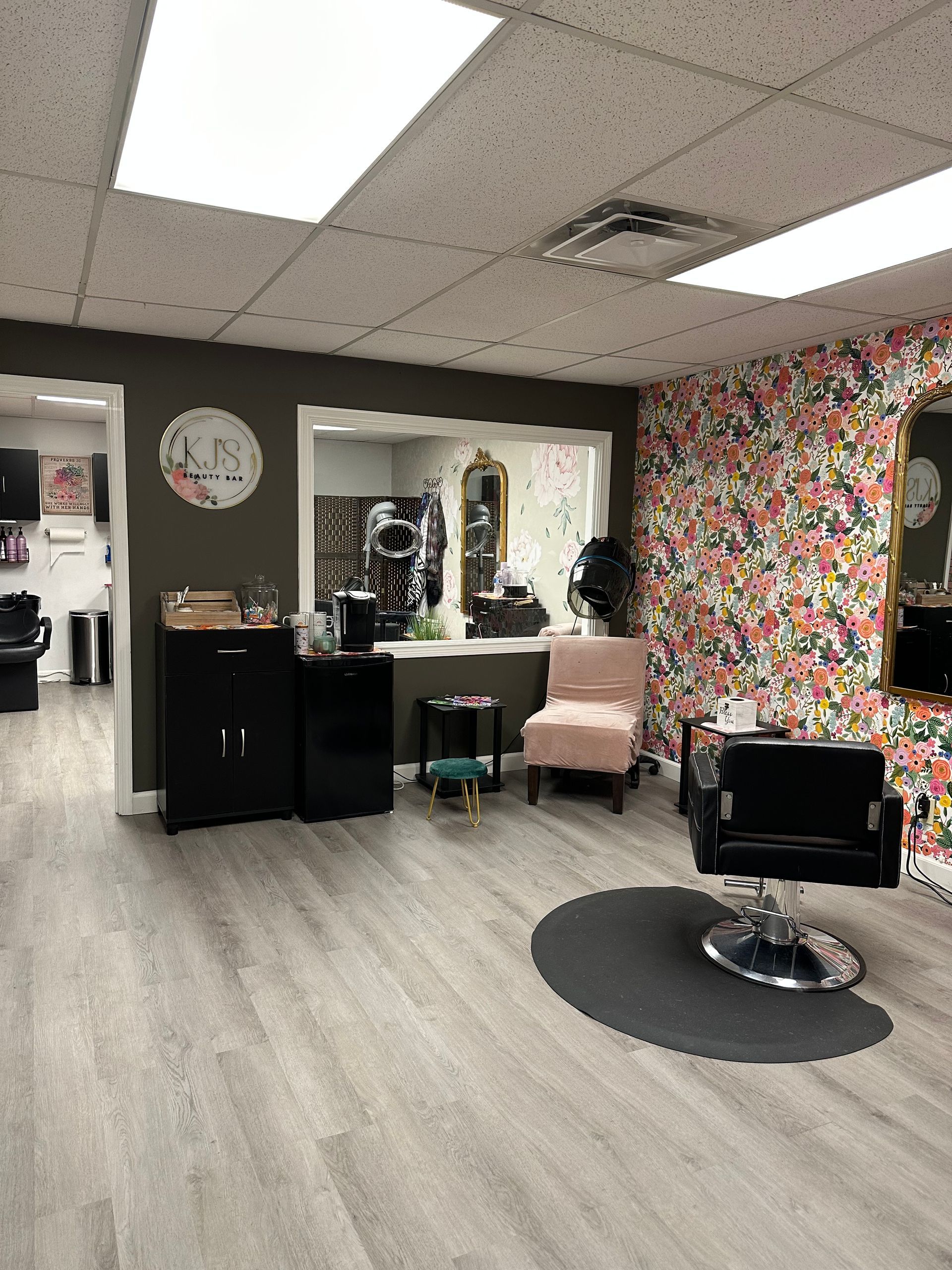 Modern salon interior with styling chair, mirrors, floral wallpaper, and light wood flooring