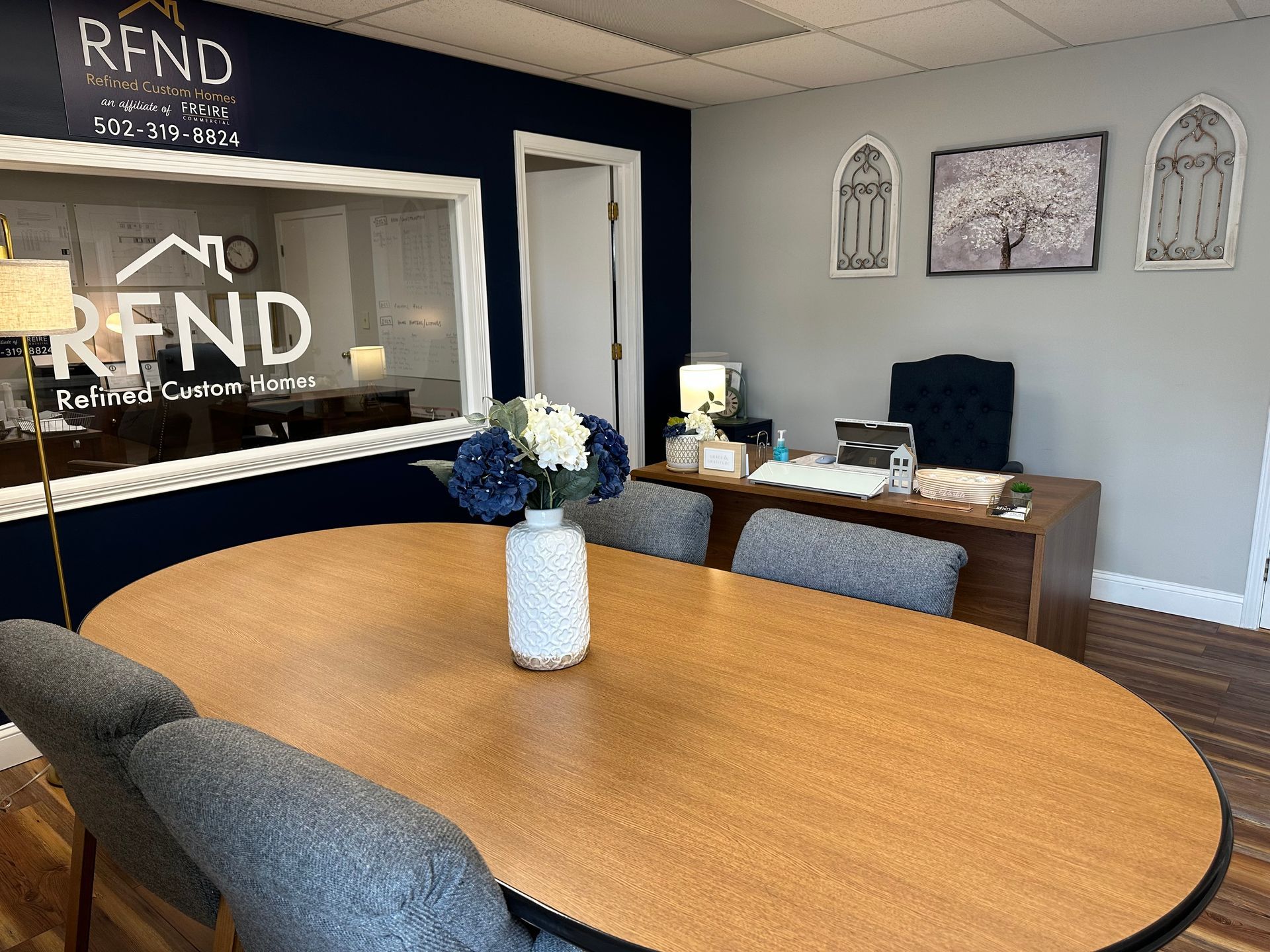 Modern office conference room with oval wooden table, gray chairs, and reception desk in the background