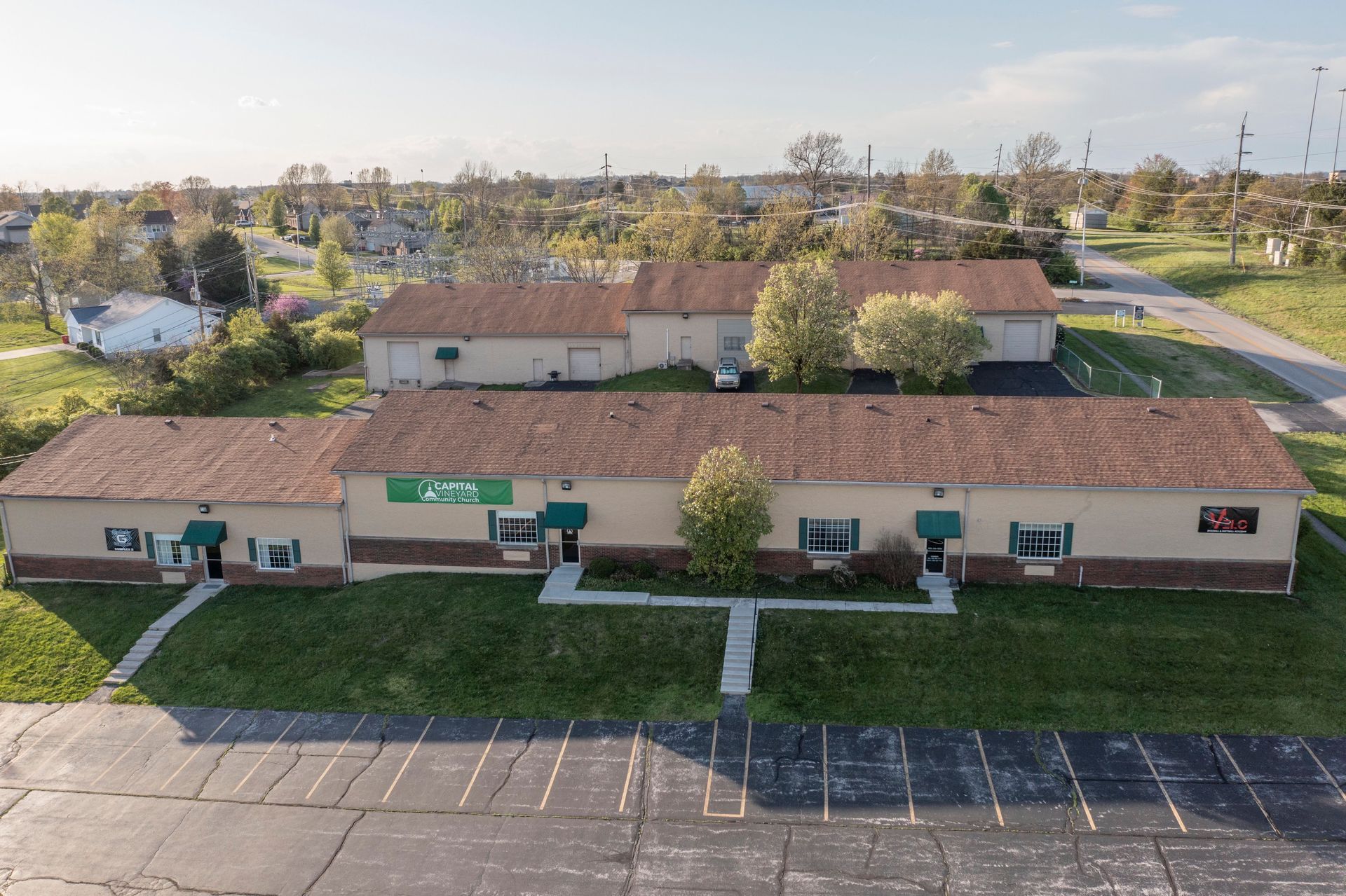 A low tan building with a red roof beside an empty parking lot, seen from above.