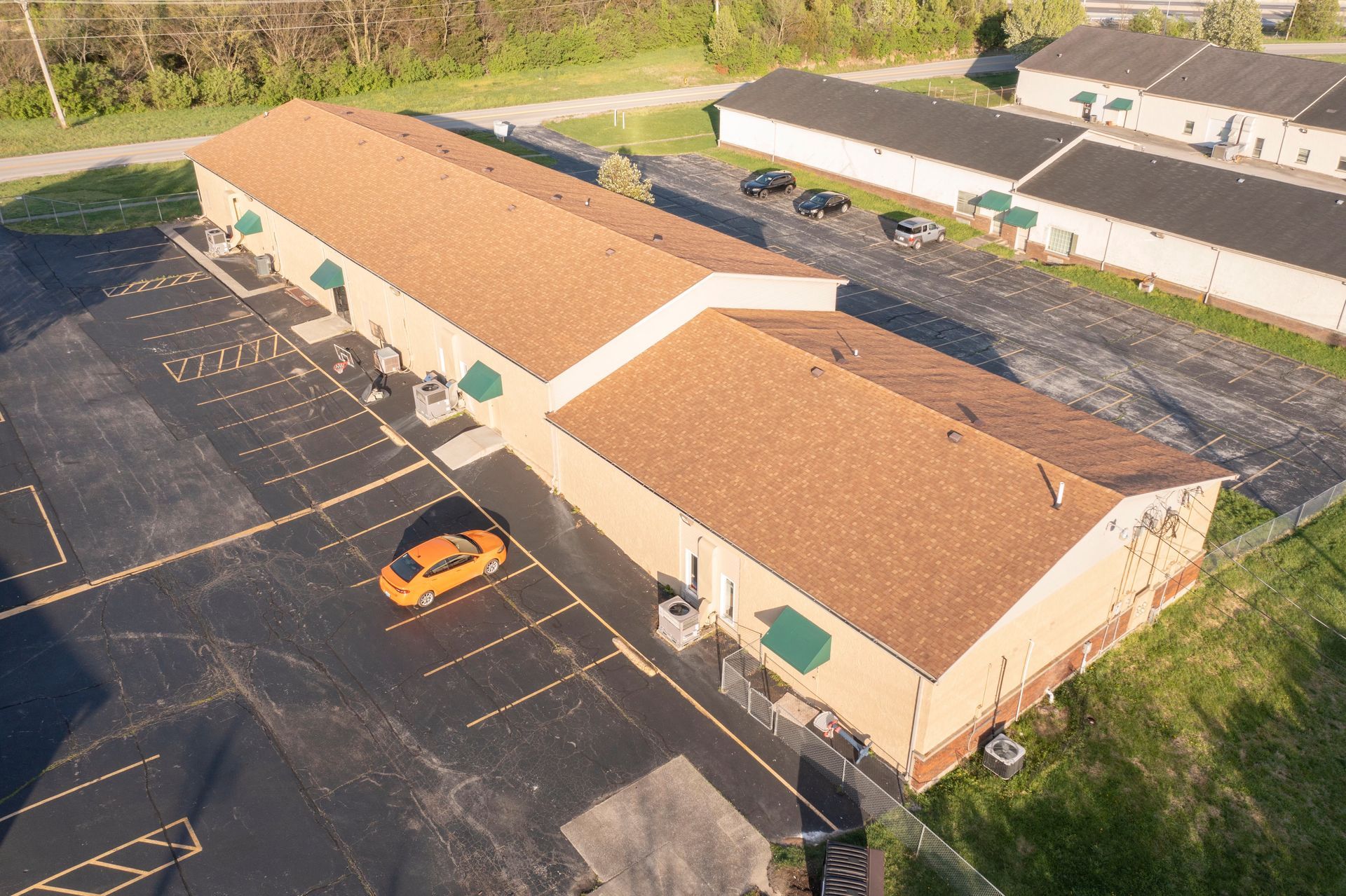 Aerial view of a beige building with a red roof beside a mostly empty parking lot with one orange car.