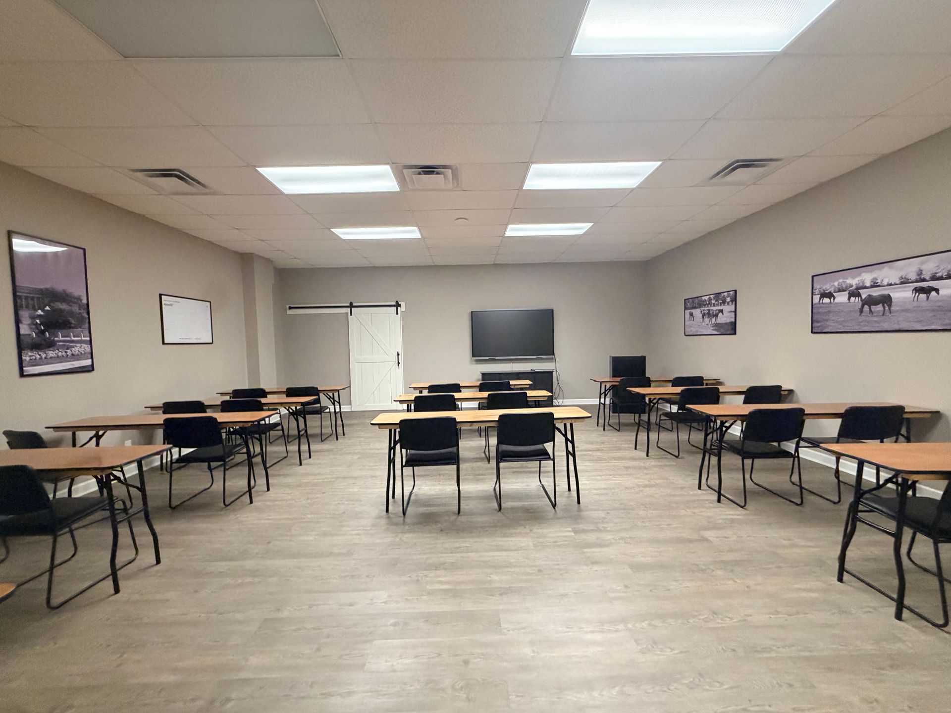Empty classroom with desks, chairs, and a large screen at the front under fluorescent lights