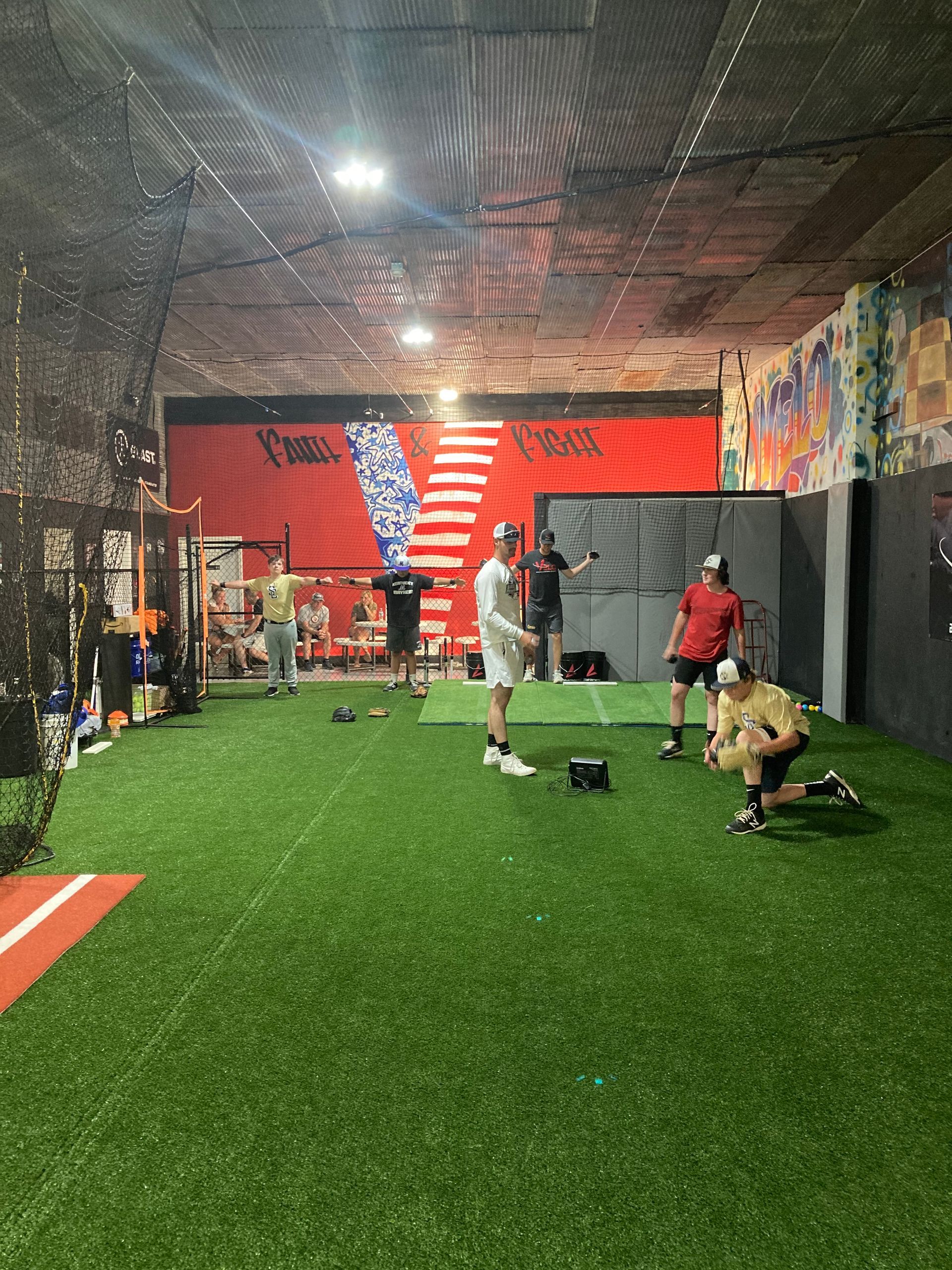 Indoor turf training area with people stretching and exercising under bright lights.