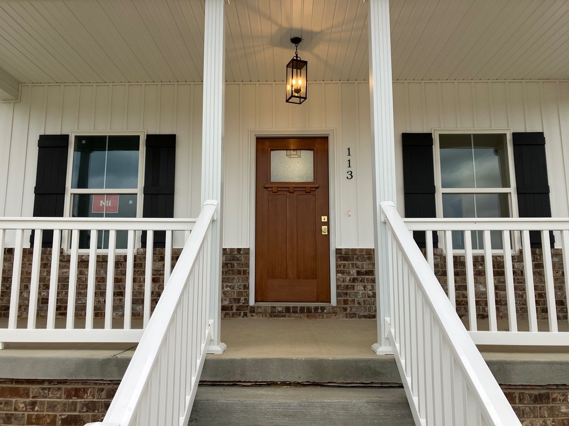 Front porch with wooden door, white railings, and black shutters on a brick house.