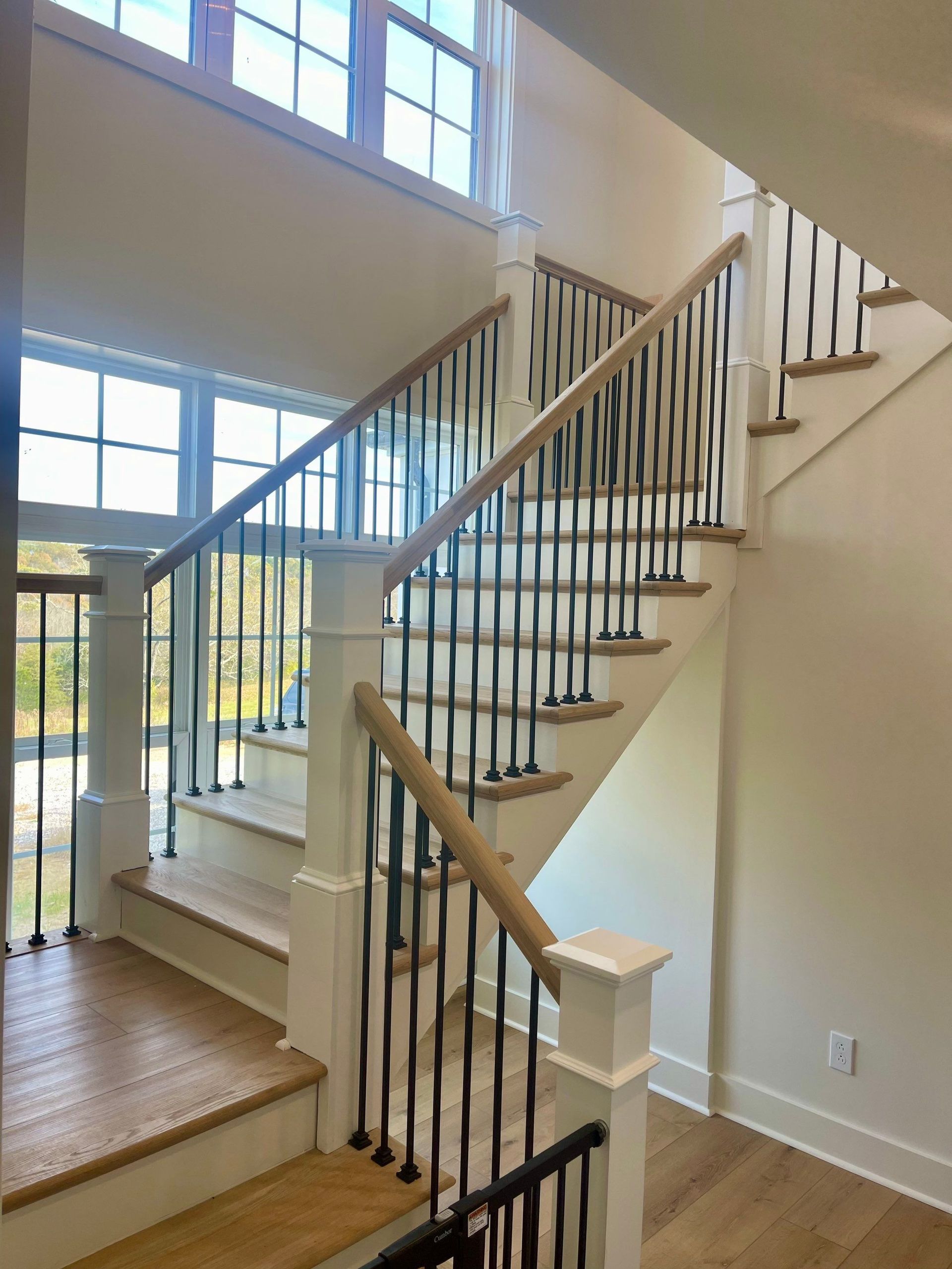 Bright stairwell with white walls, wooden steps, black balusters, and large windows letting in daylight