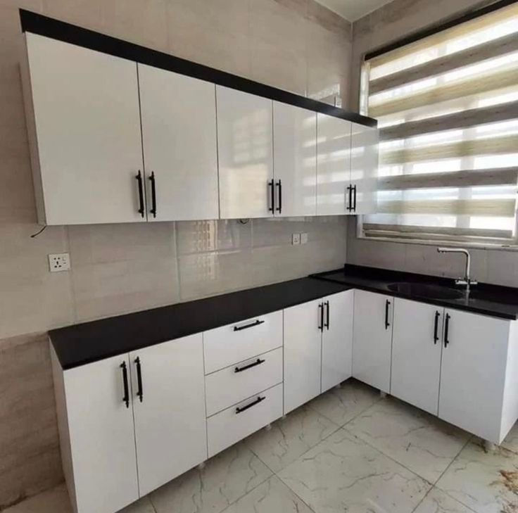 Cocina moderna con armarios blancos, encimeras negras y paredes y suelo de azulejos beige.