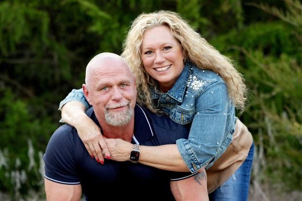 Smiling couple outdoors, woman hugging man from behind in a green setting