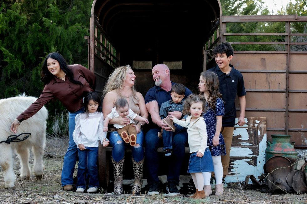 Family sitting with two goats in front of a barn, smiling children and adults gathered outdoors