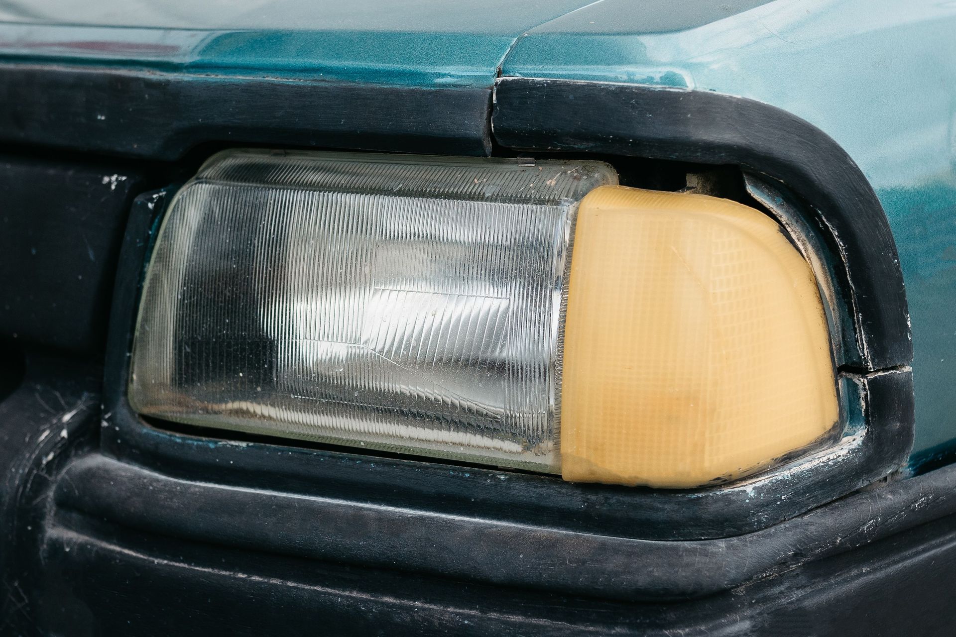 Close-up of a car headlight with a yellow turn signal lens and blue-green hood