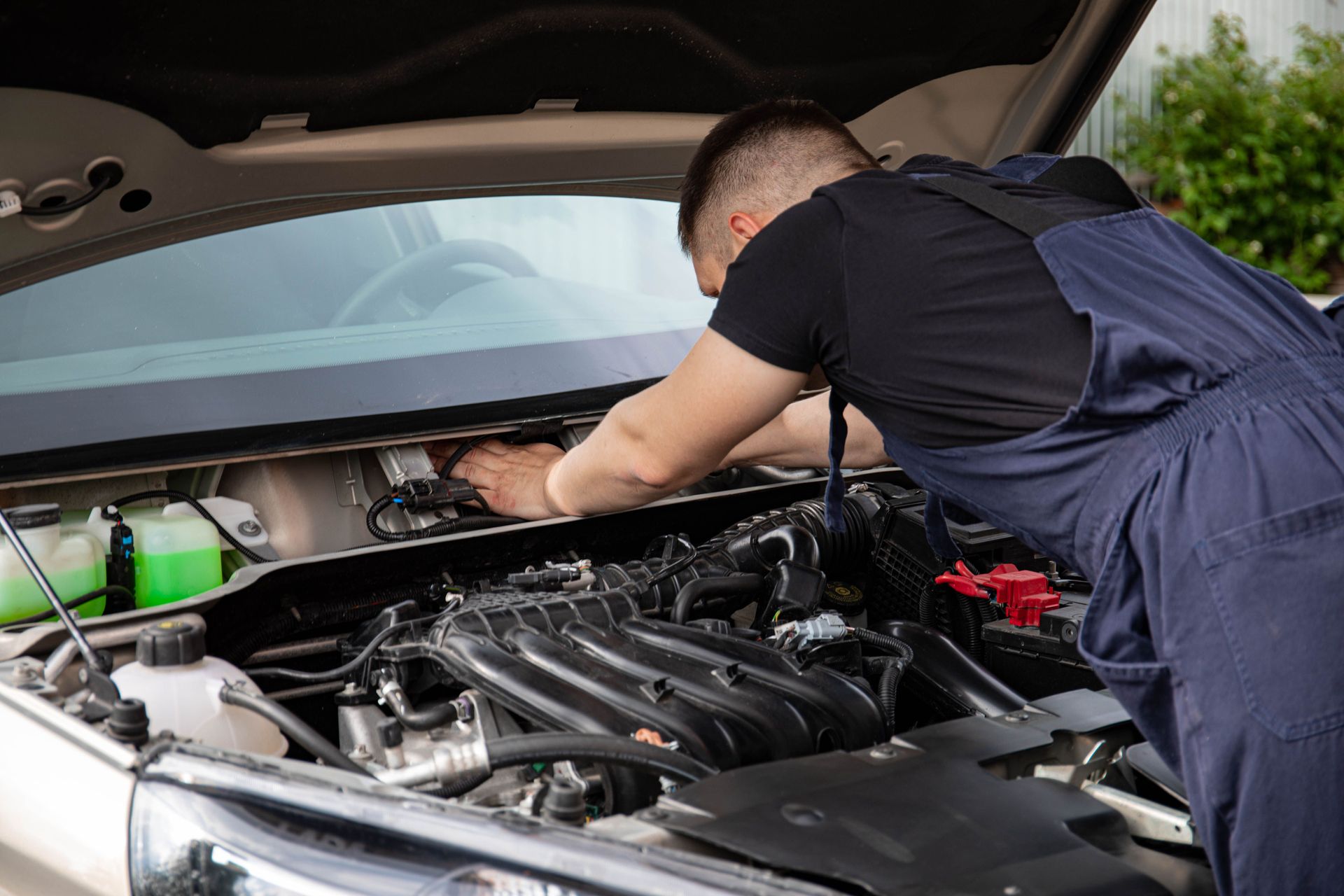 Mechanic working under a car hood in a garage, inspecting the engine bay
