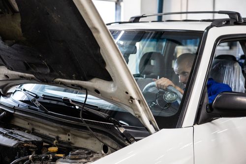 Mechanic working under the hood of a white car in a garage