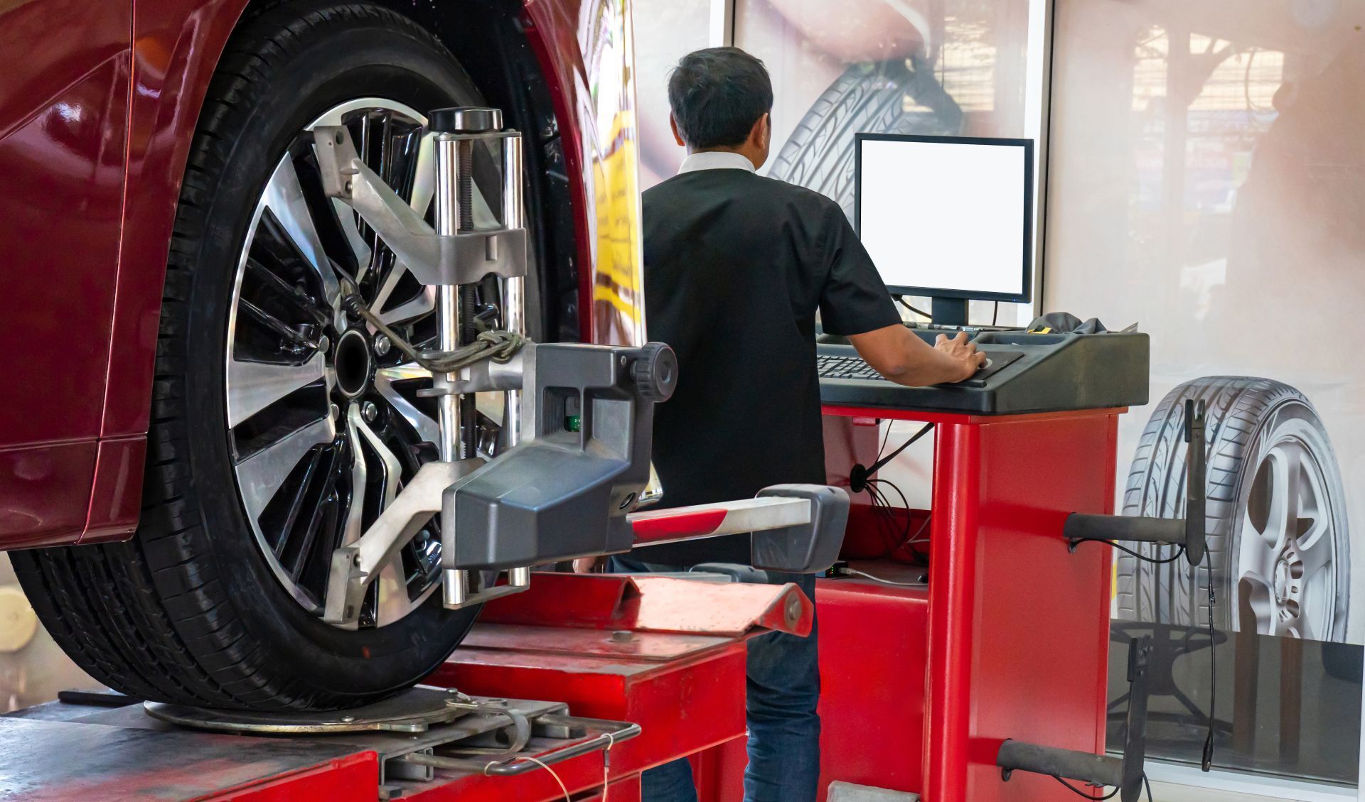 Vehicle wheel alignment in a workshop, with a mechanic using a computer beside a raised car wheel.