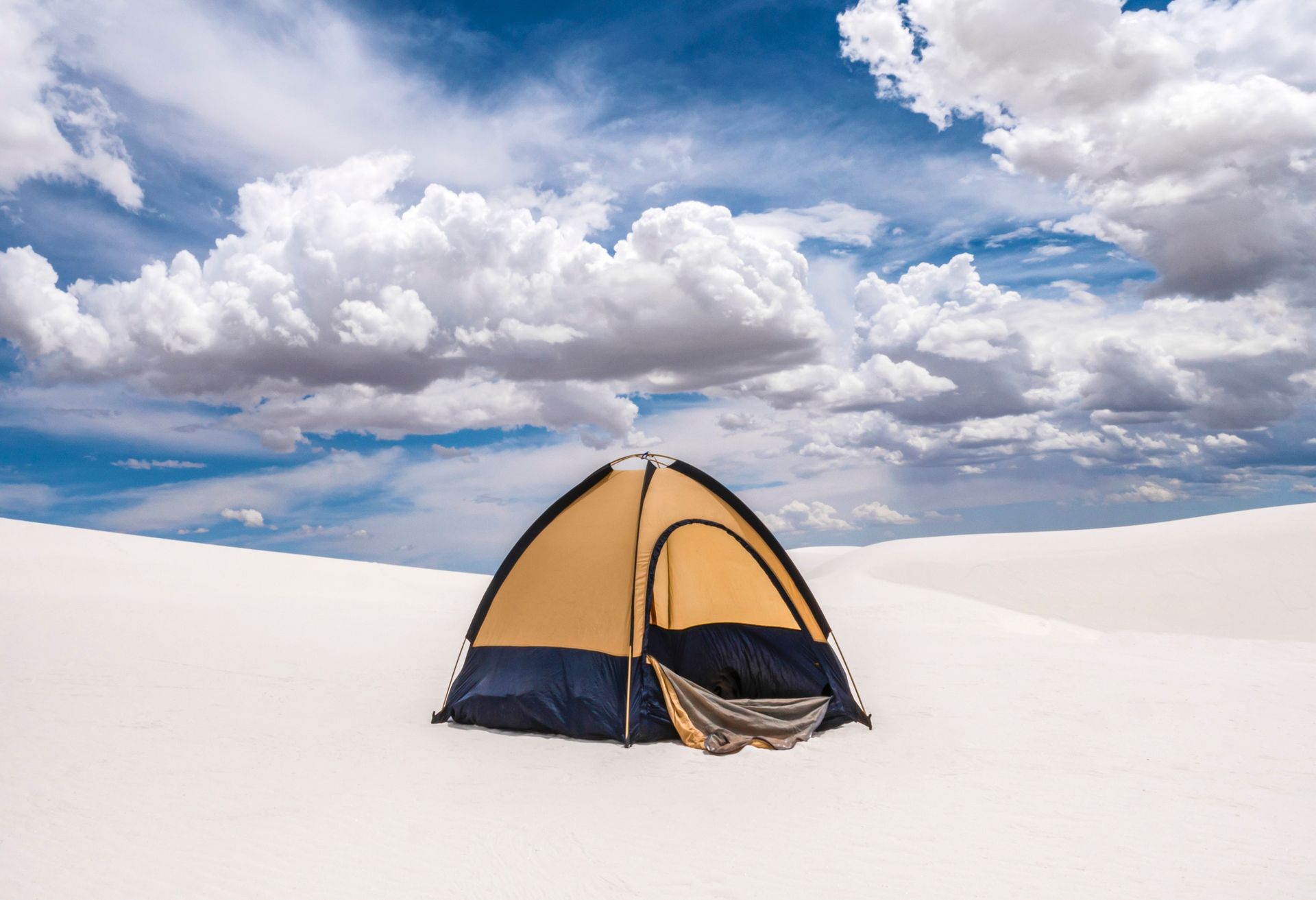 Yellow-and-blue tent on a bright white salt flat under a cloudy blue sky
