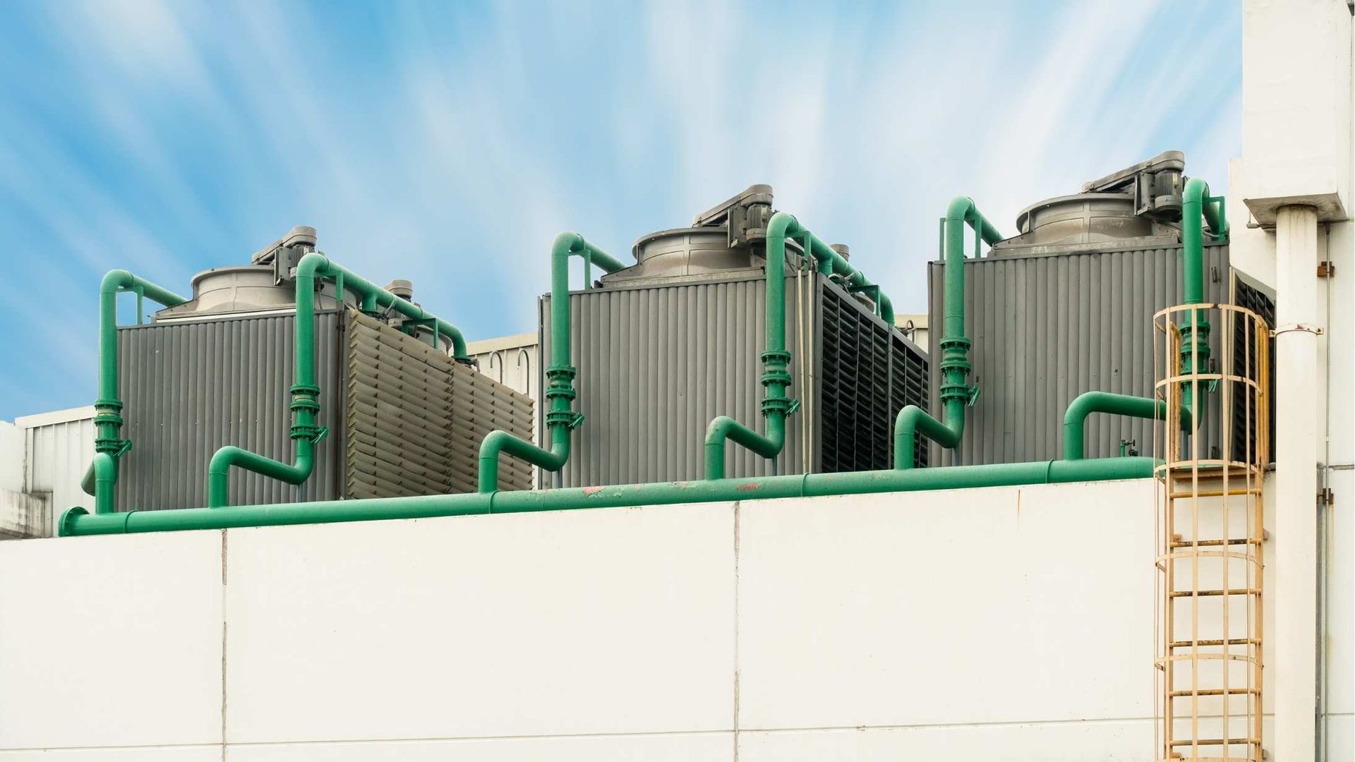 A row of cooling towers on top of a building with green pipes.