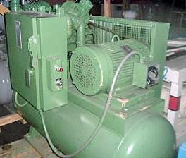 A green air compressor with a motor attached to it is sitting on top of a wooden table.