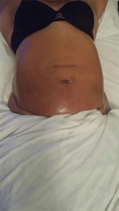 A woman in a black bra is laying on a bed with her stomach showing