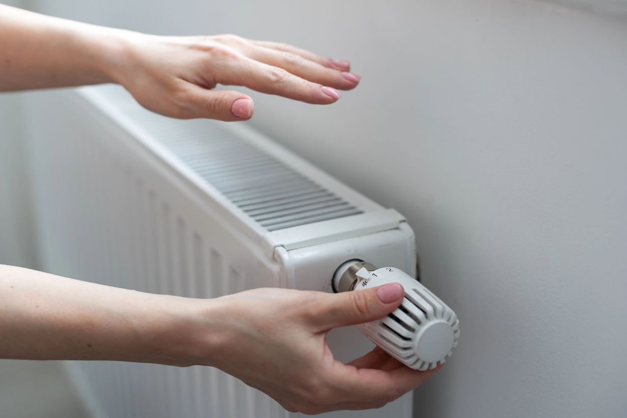 Mani che regolano la manopola bianca del termostato di un termosifone a parete.